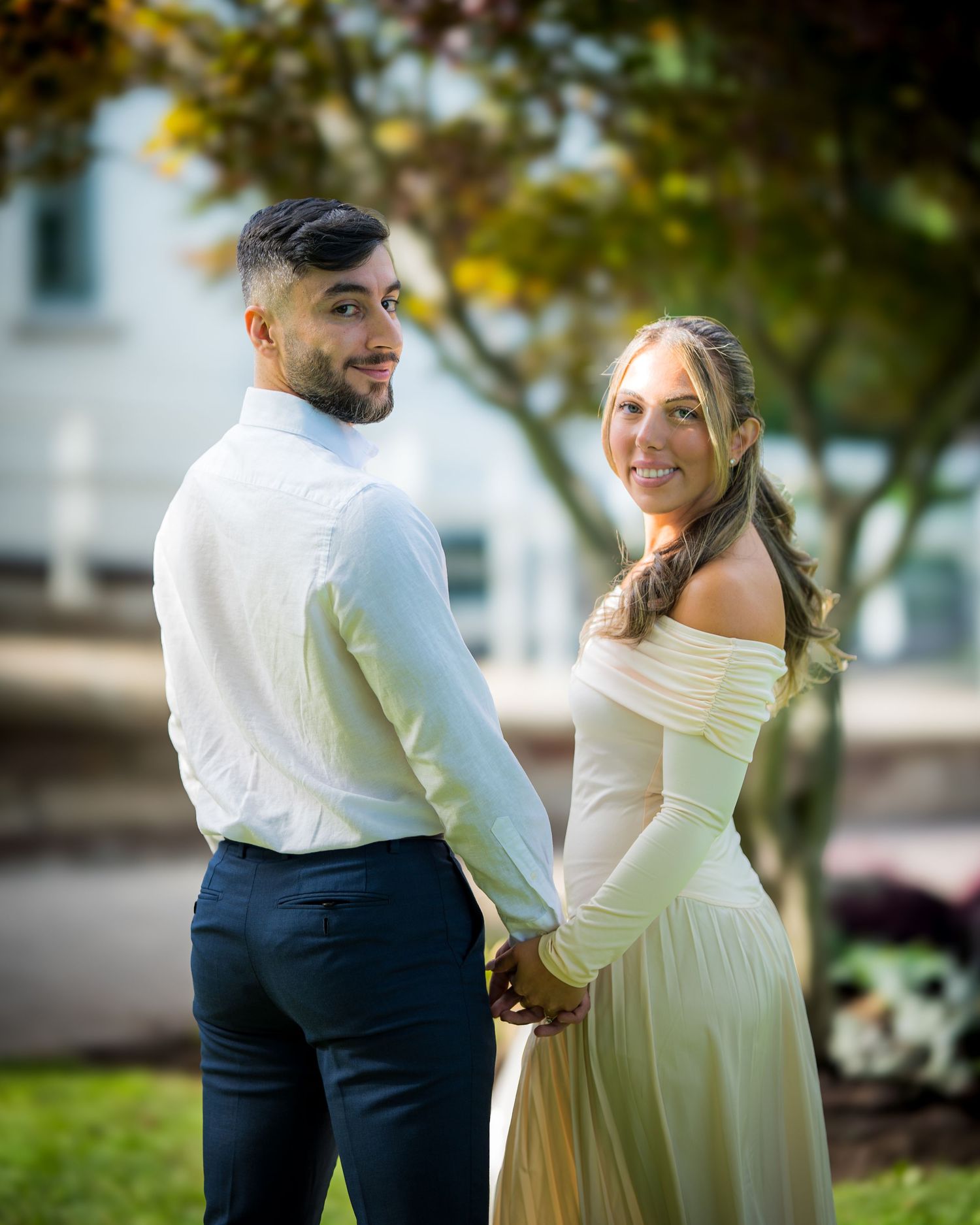 Couple sharing tender moment in casual formal wear against autumn trees.