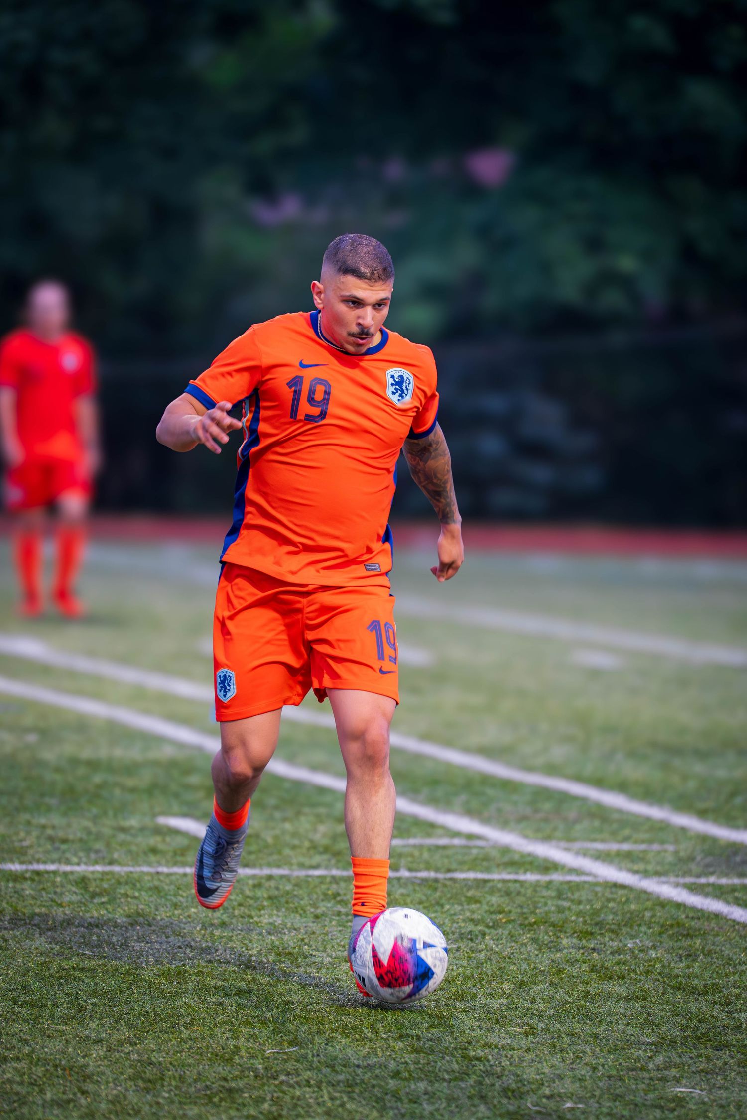 Soccer player in orange jersey number 19 dribbles ball across field.