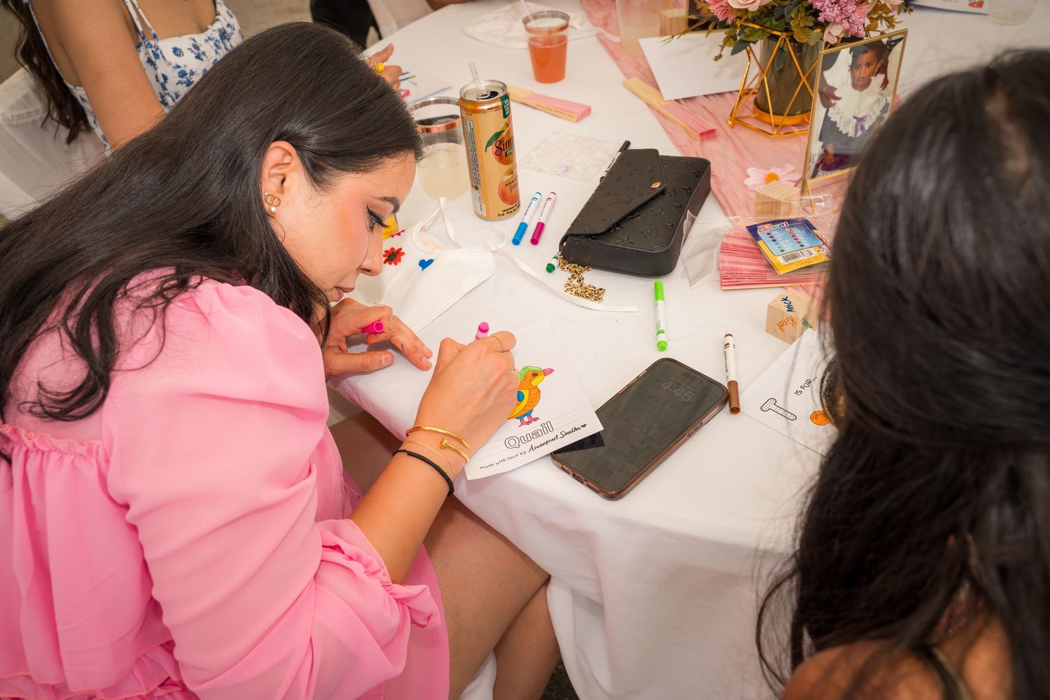 People working on craft projects at table with pink tablecloth.
