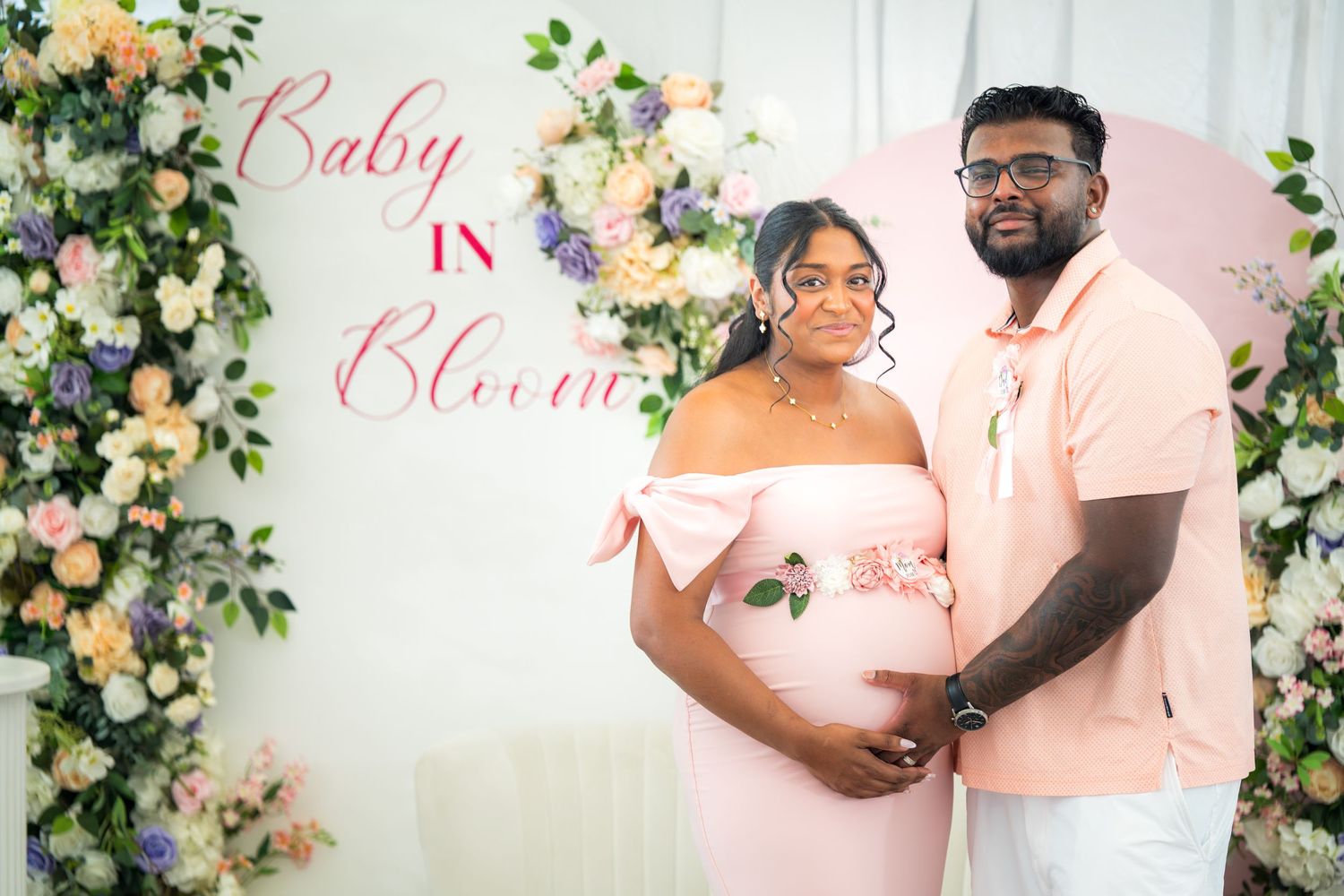A couple embraces in front of a romantic floral backdrop with pink and peach blooms.
