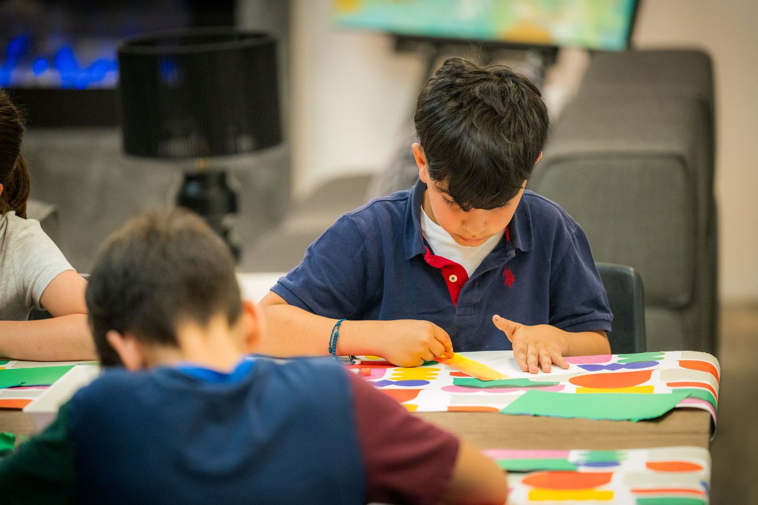 Boy in blue polo shirt focuses on colorful paper craft at an art activity table.