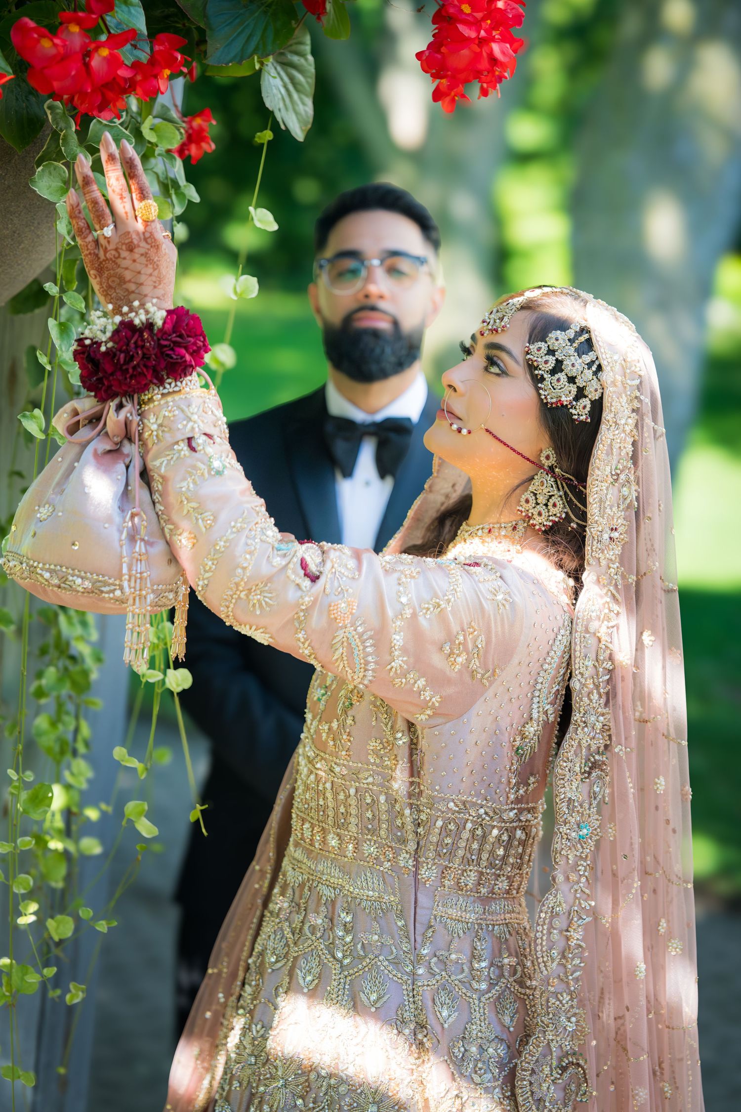 Elegant couple in traditional South Asian wedding attire pose under floral decorations in an outdoor garden setting.