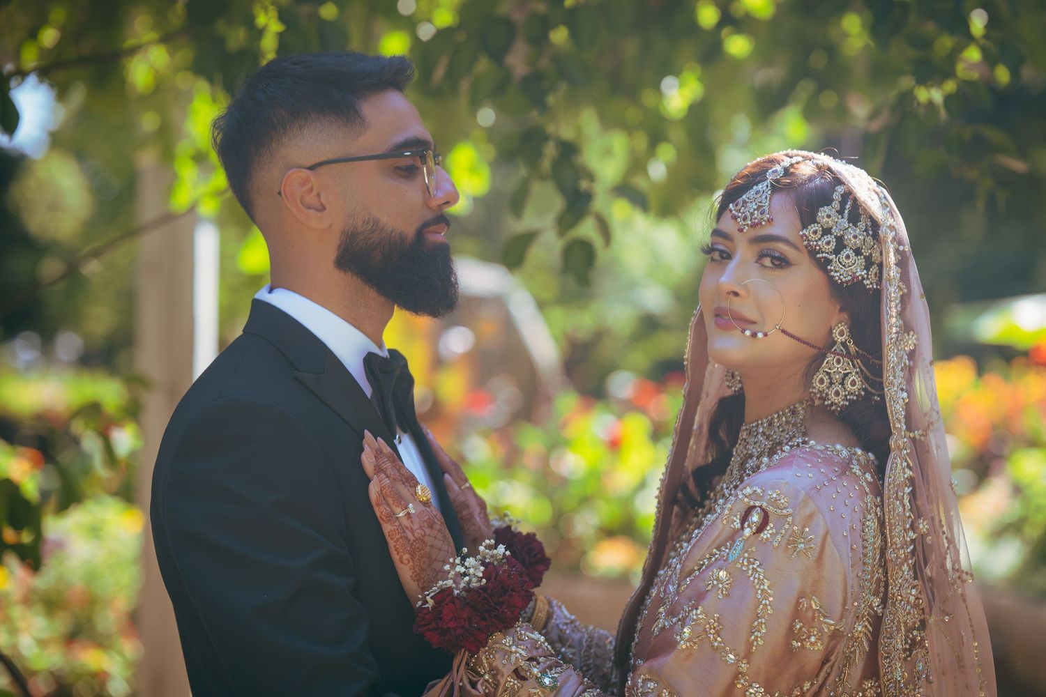 Newlyweds in traditional South Asian wedding clothes share intimate moments during outdoor photoshoot.