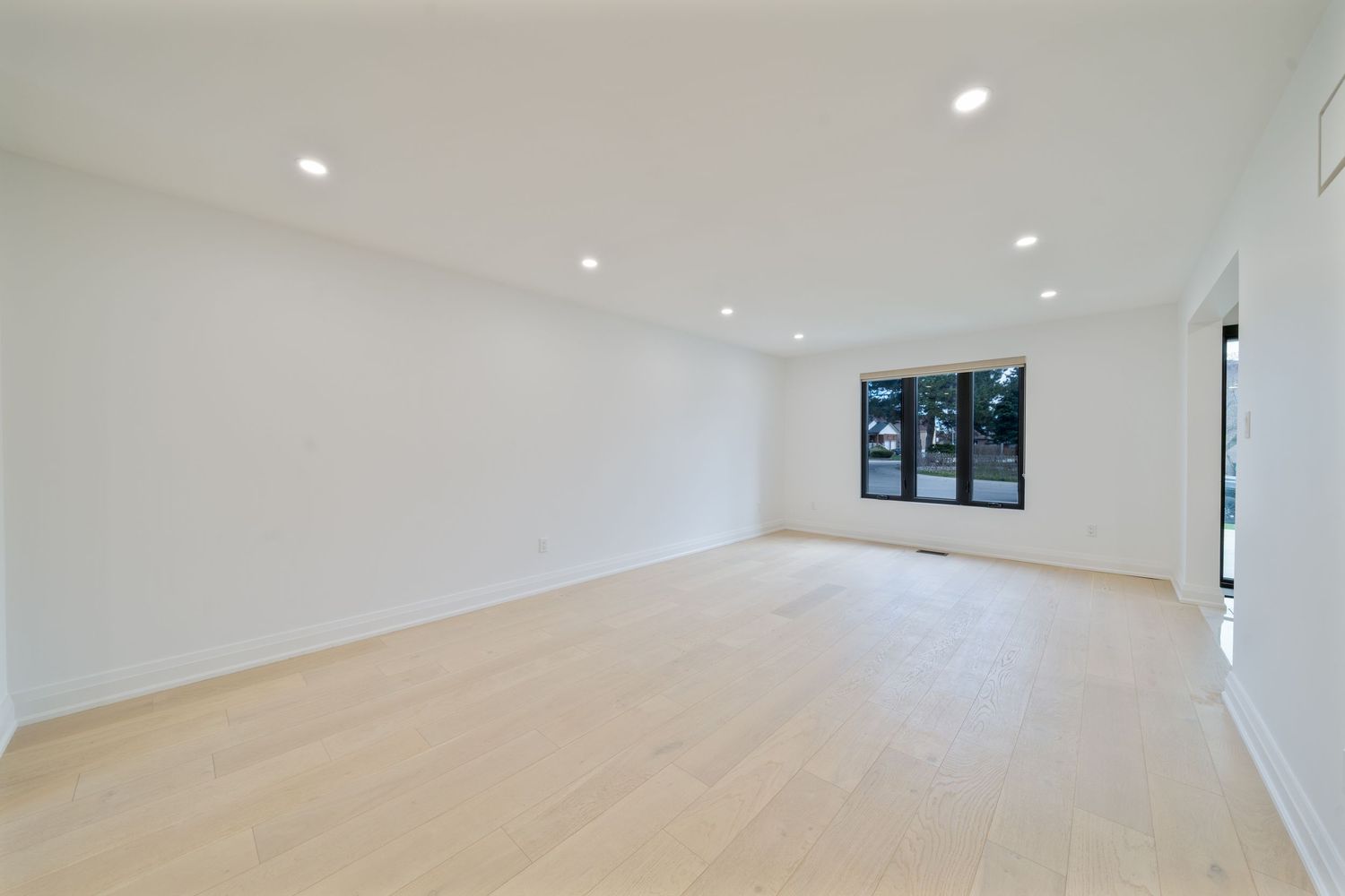 Modern white hallway with recessed lighting and hardwood flooring leads to a bright open space.