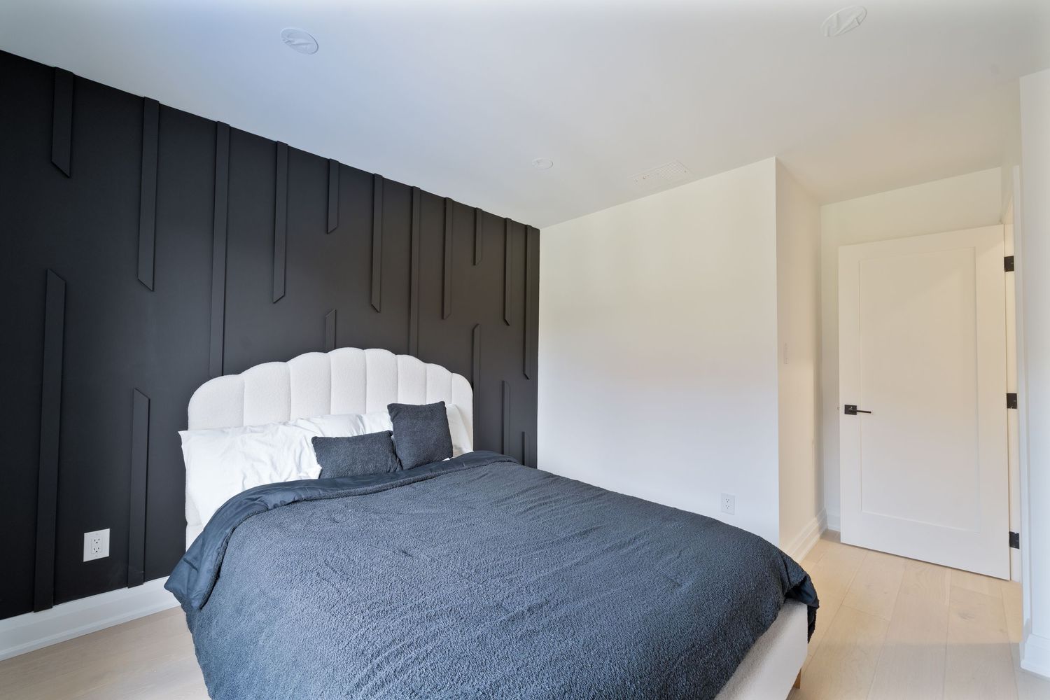 Modern bedroom features a dramatic black accent wall contrasting with white walls and gray bedding.
