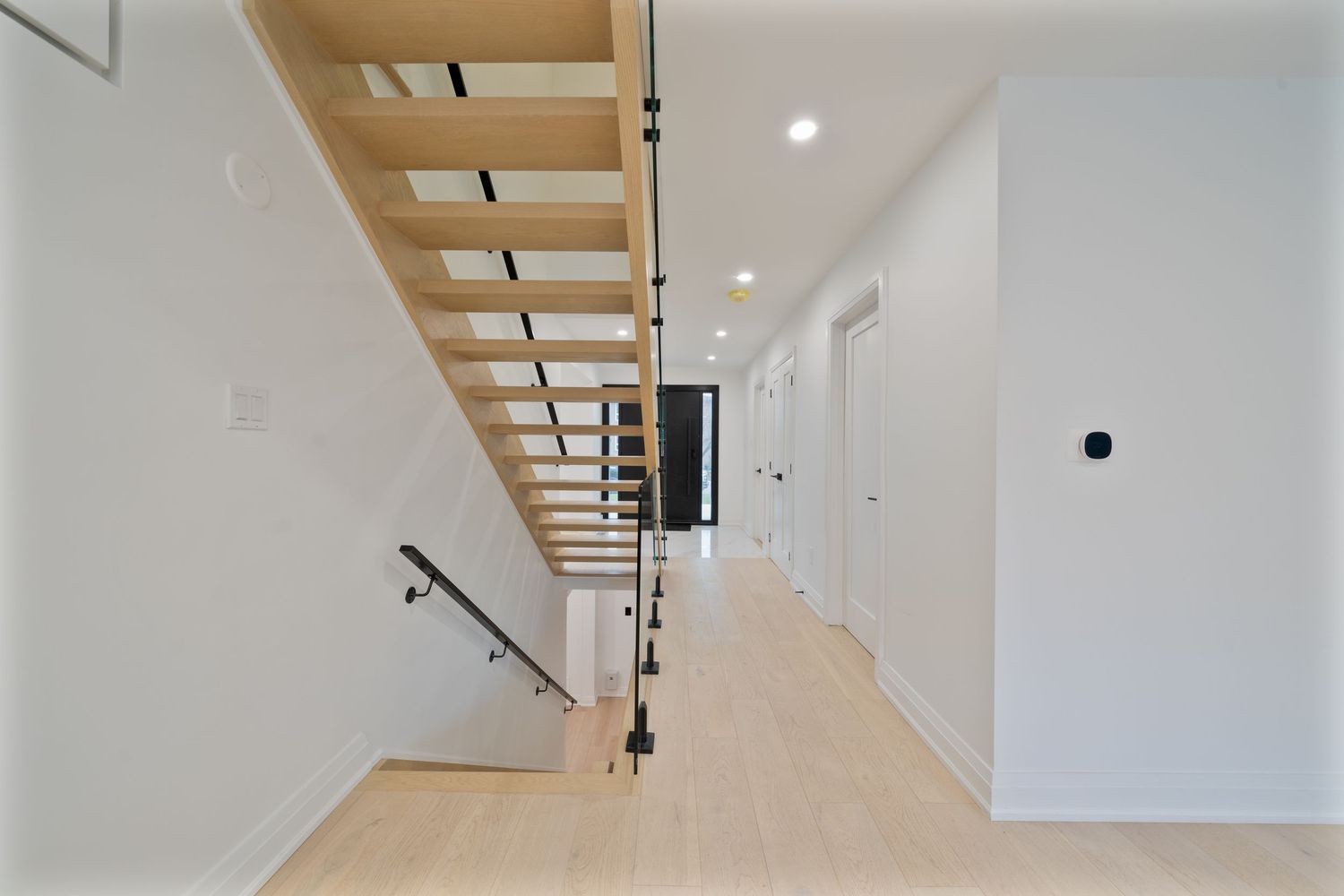 Modern white staircase with wooden treads and glass railing in a minimalist interior space.