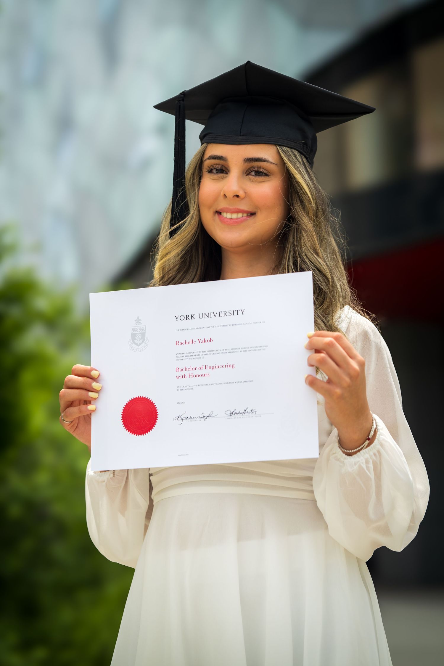Graduate displays York University diploma while wearing academic regalia outdoors.