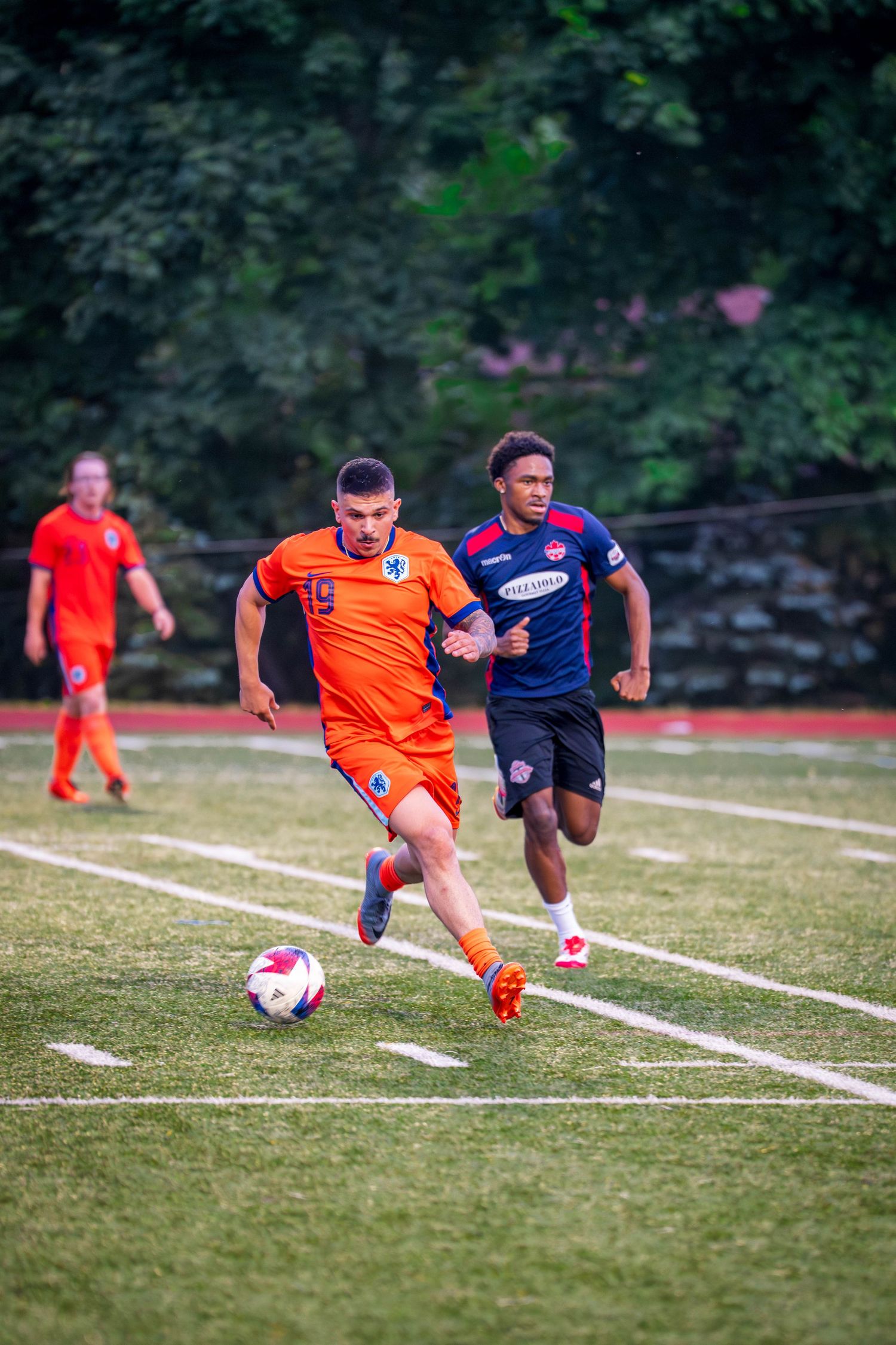 Soccer player in orange jersey dribbles ball past defender during competitive match on grass field.