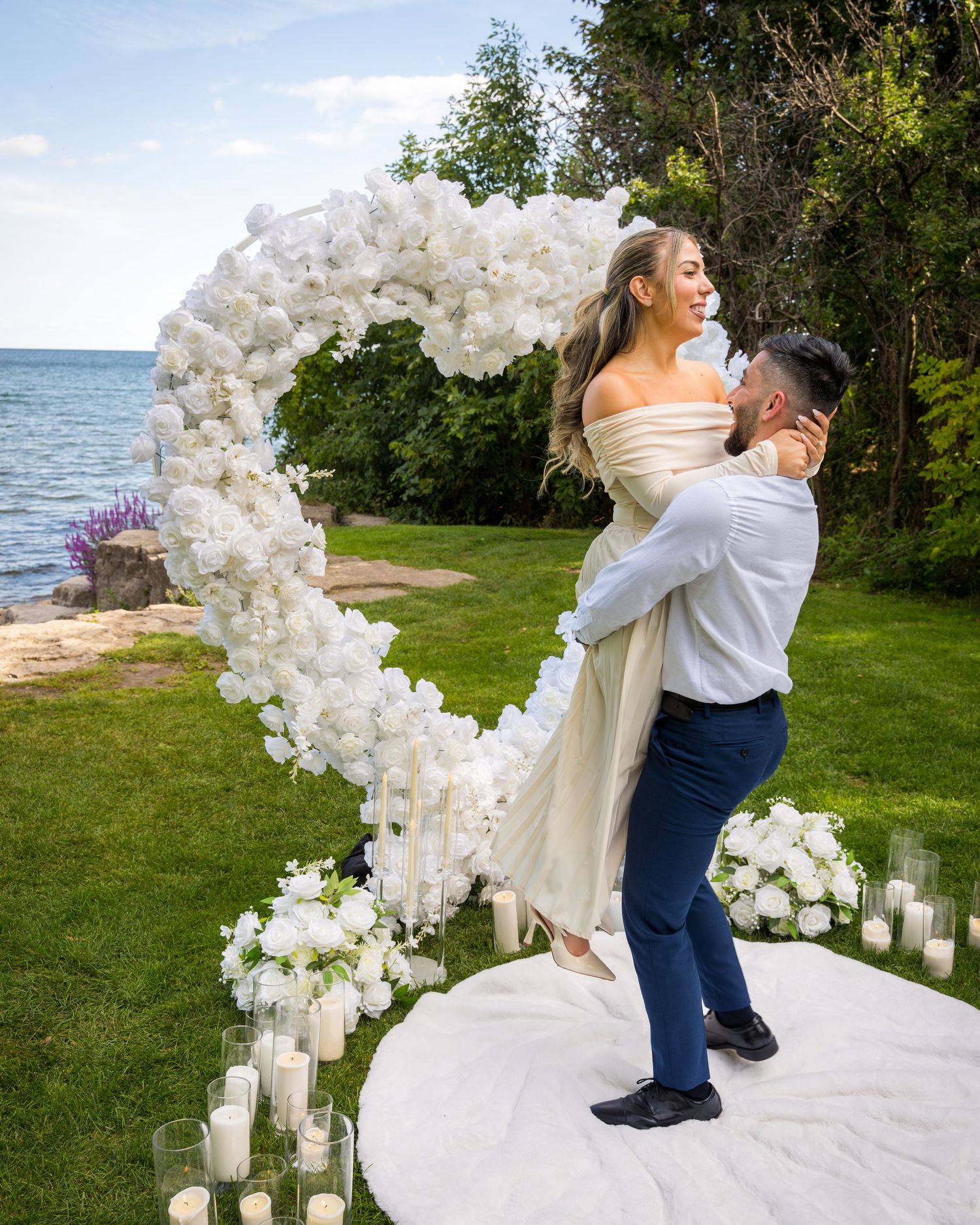 A romantic moment captured under a white floral arch with candles on the ground.