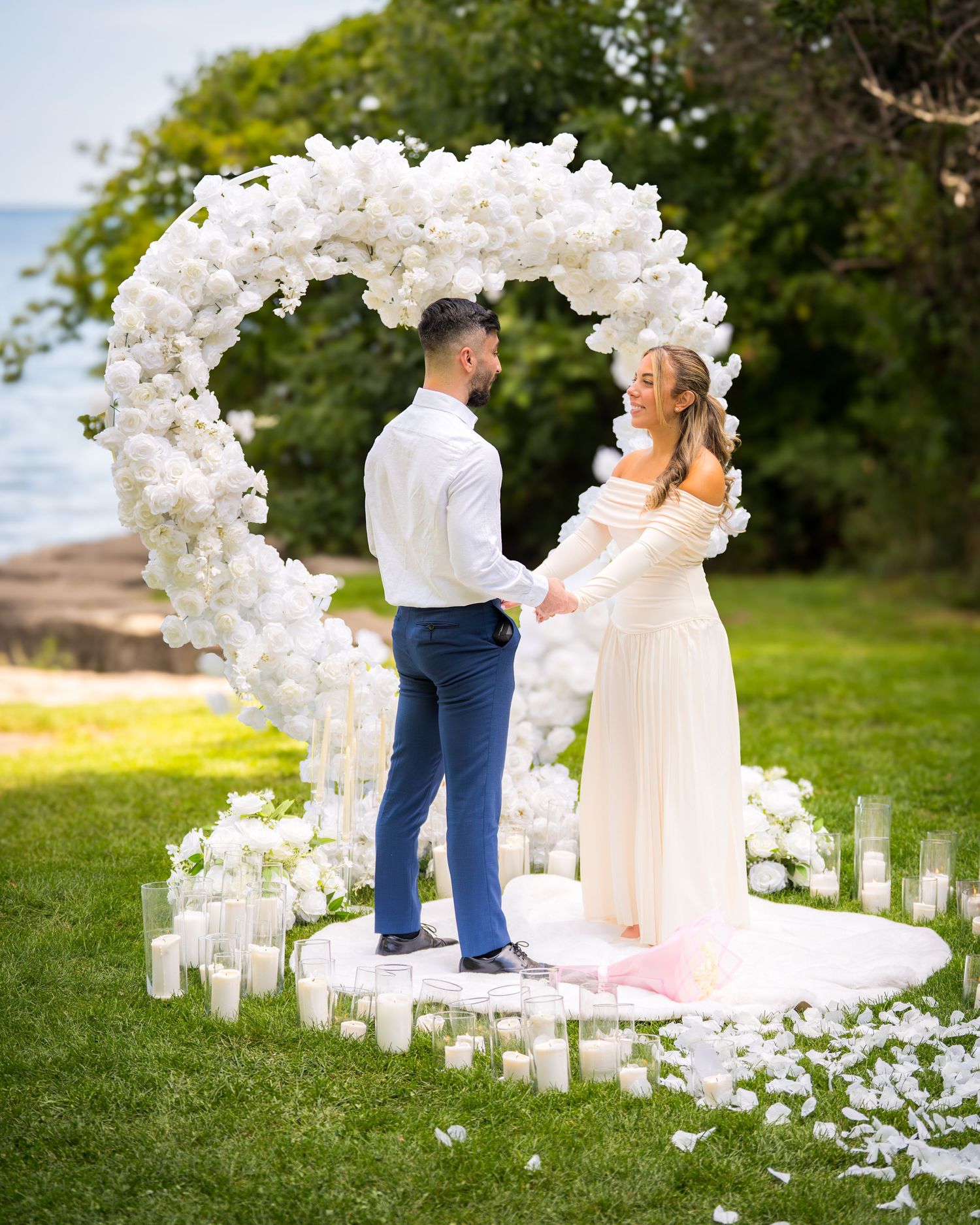 An outdoor wedding ceremony space decorated with white orchid arch and glowing candle arrangements.