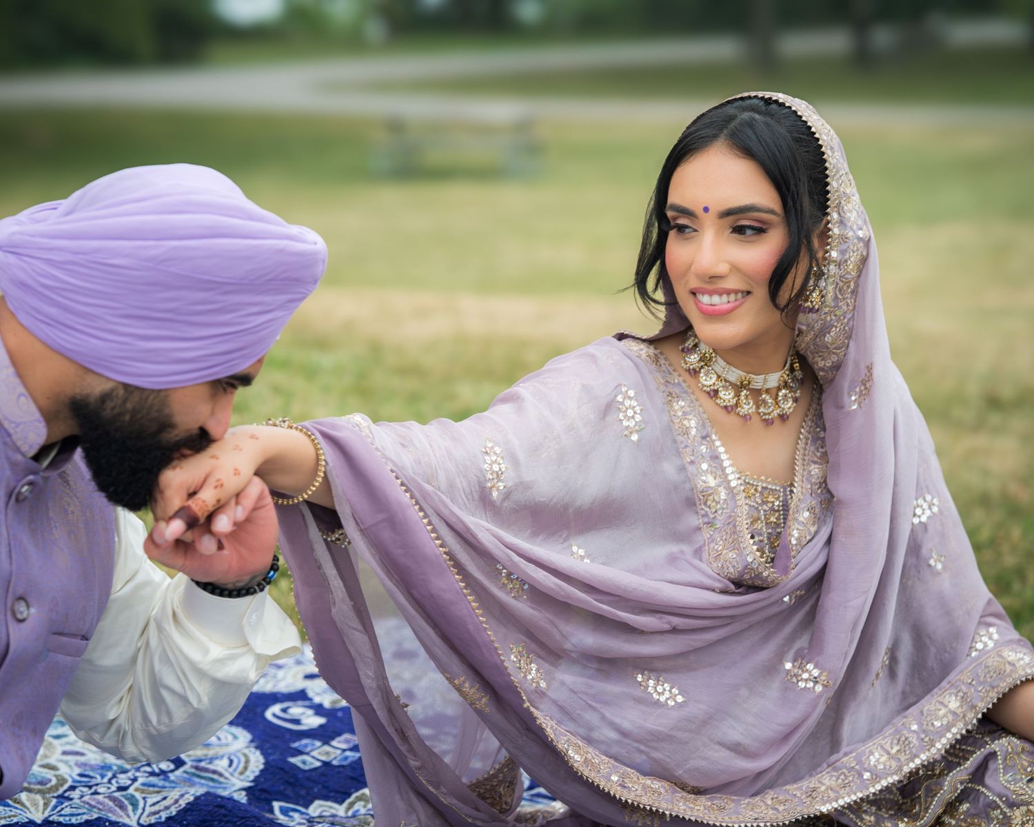 Traditional wedding couple in lavender and white attire posing with decorative blue textile.
