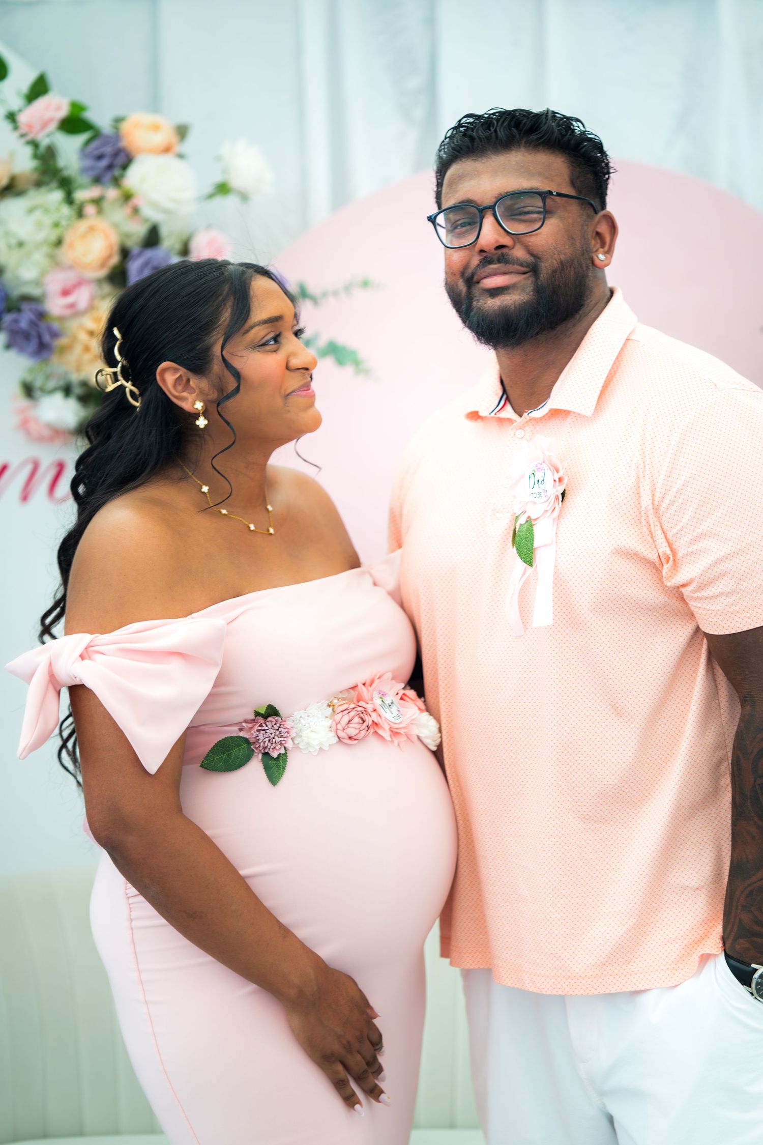 Couple shares intimate moment at baby celebration with pink floral decor and matching attire.
