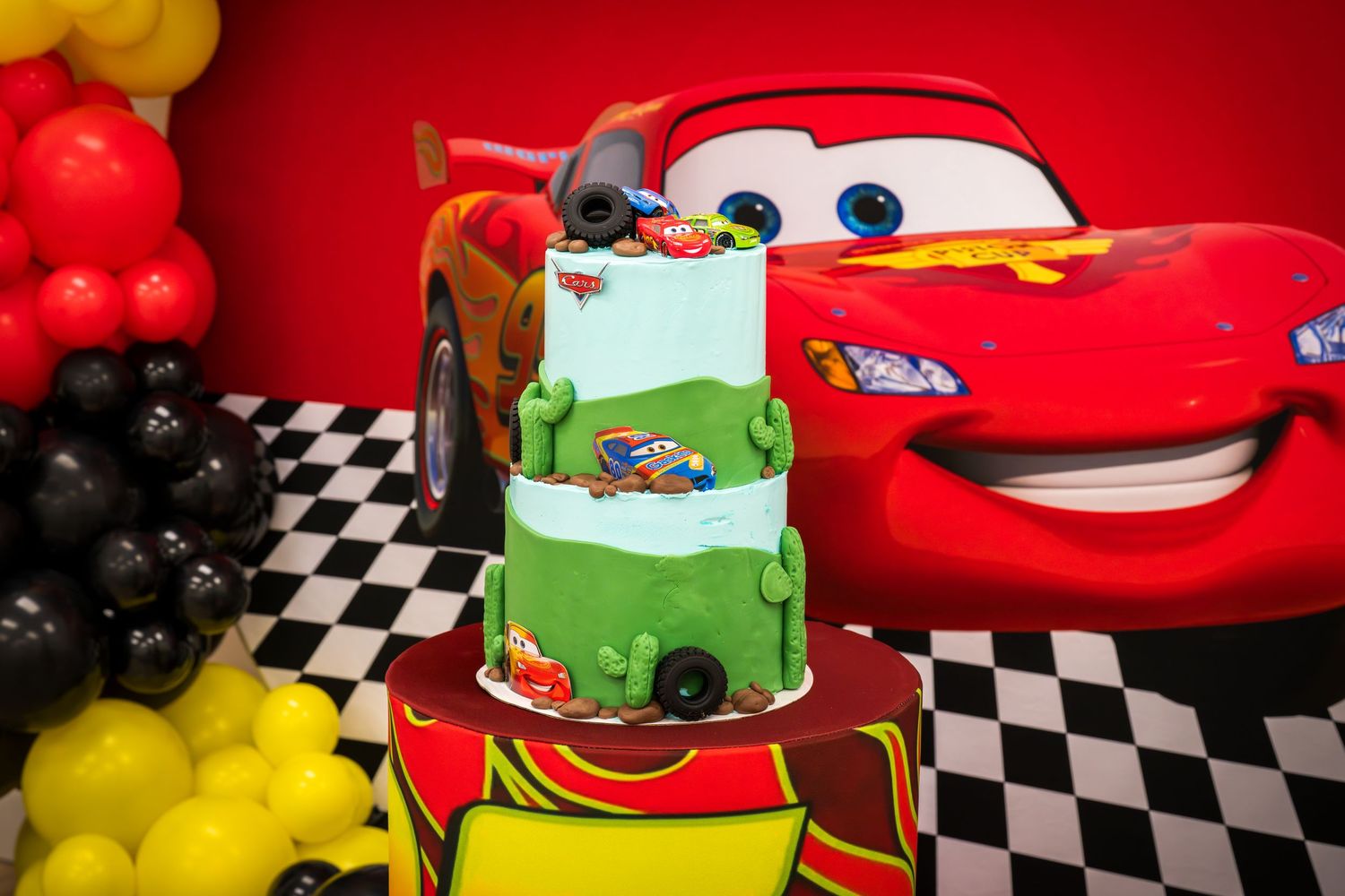Three-tier Cars themed birthday cake featuring Lightning McQueen decorations and characters.