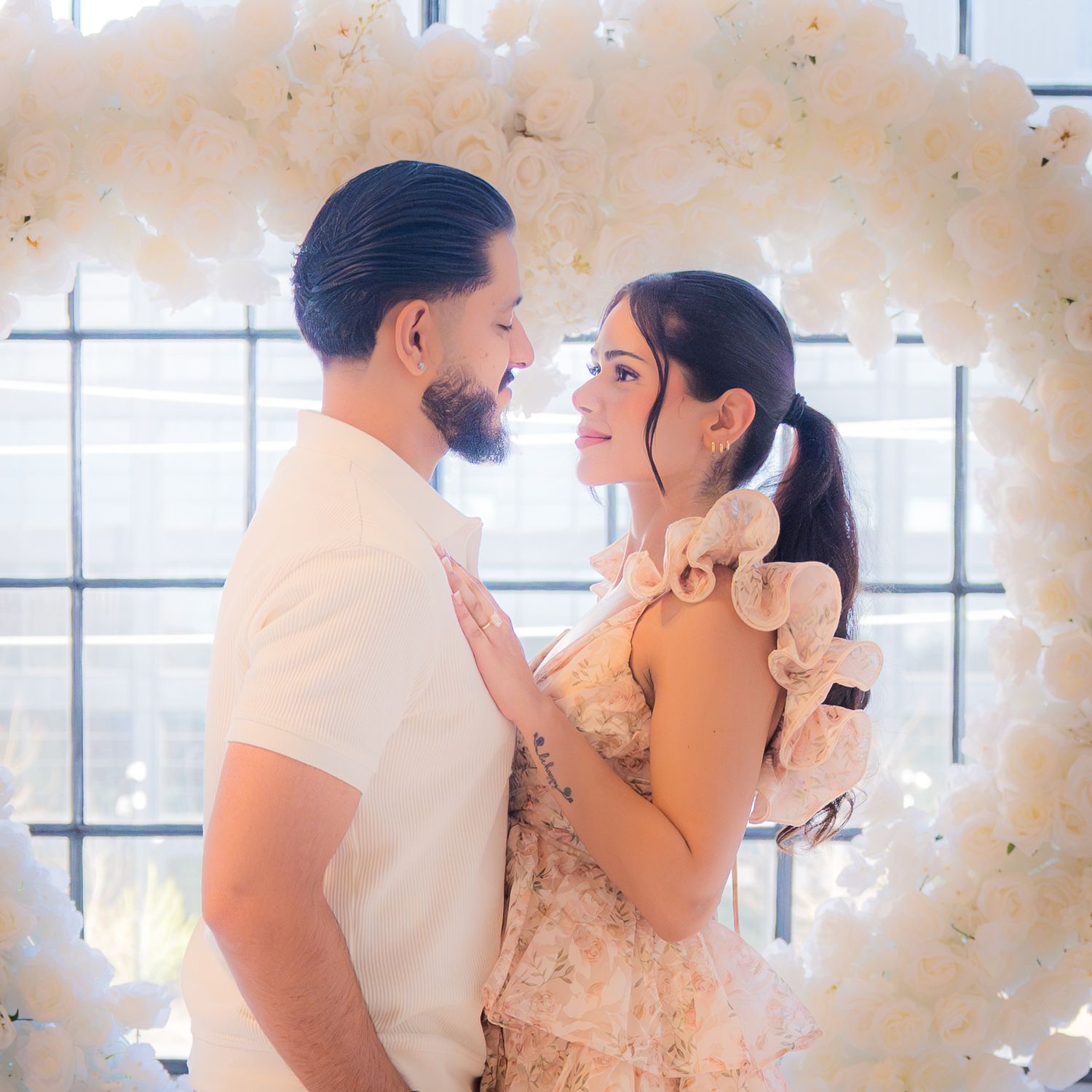 Couple gazing at each other tenderly framed by a stunning white floral heart-shaped arch backdrop.