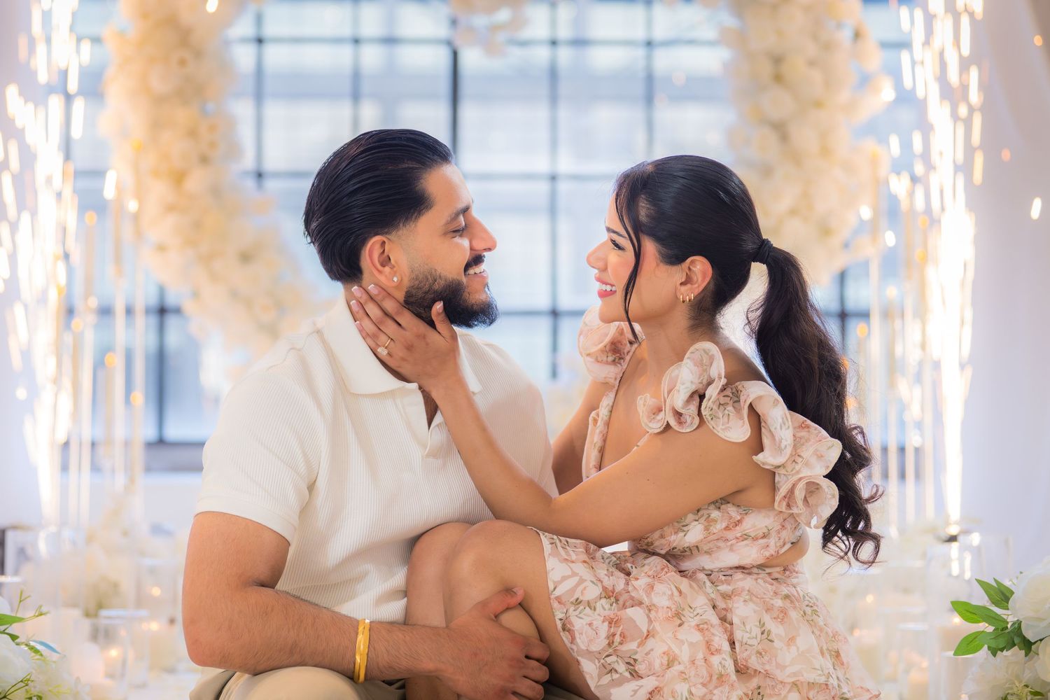 Romantic couple sitting together gazing into each other's eyes surrounded by elegant white floral decor.