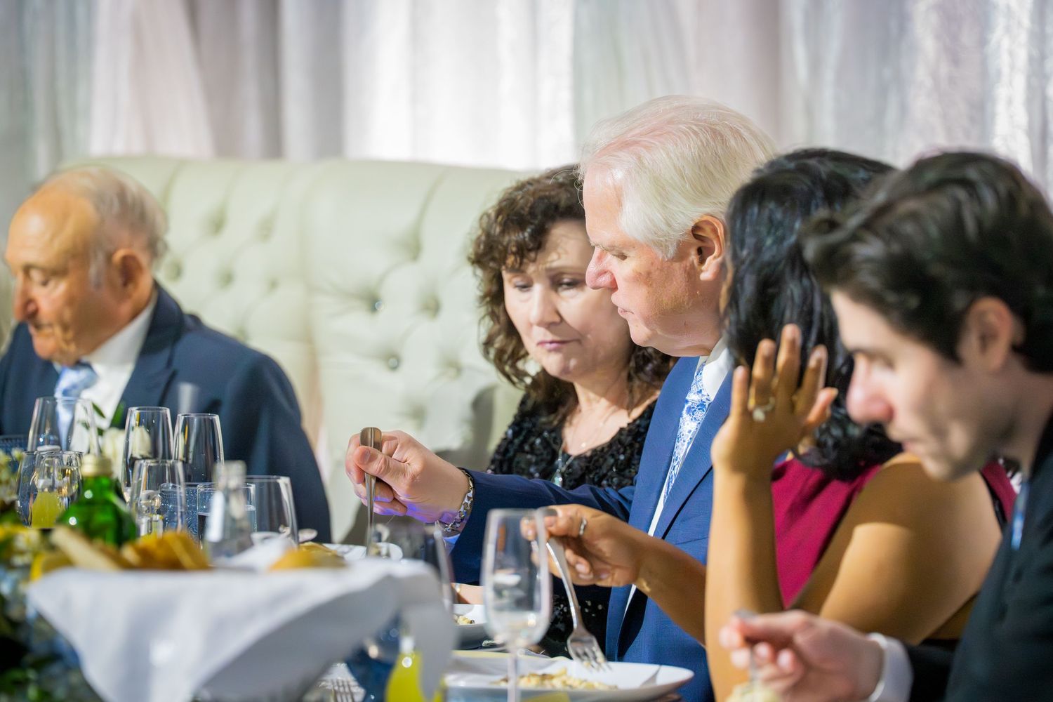 Guests socializing and dining at an elegant wedding reception with white decor and glassware.