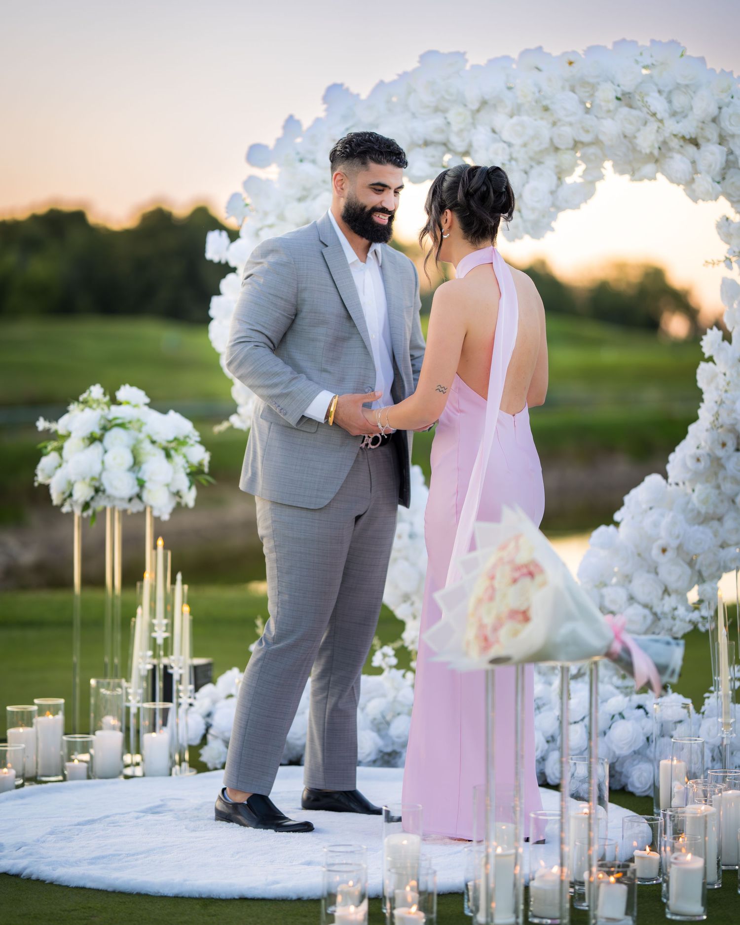 A couple celebrates their engagement under an elegant white floral arch.