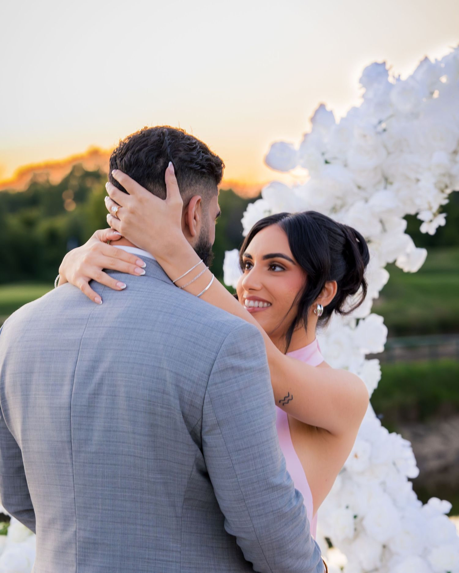 Couple embracing under white balloon arch during sunset photoshoot.