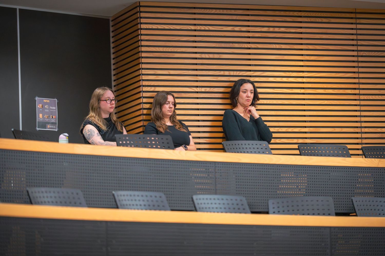 Row of black chairs against wooden slat wall in conference room setting.
