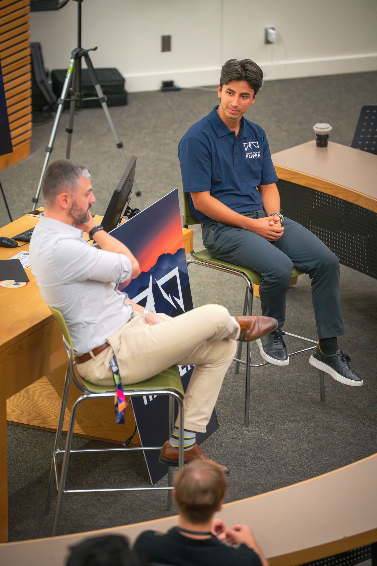Students seated in classroom chairs wearing navy blue polo shirts and khaki pants during a discussion session.