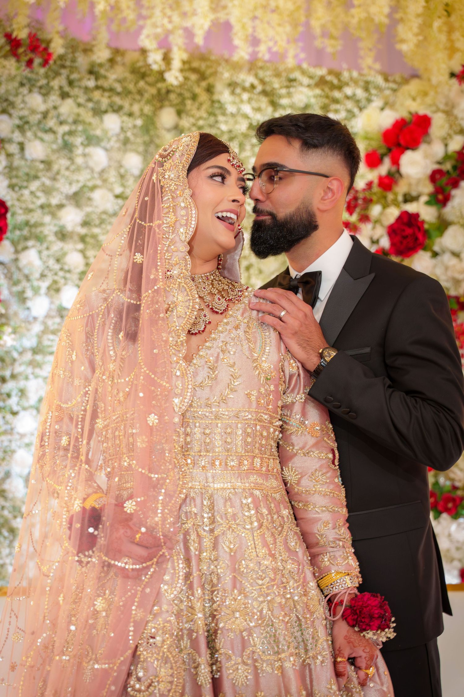 Romantic wedding photoshoot with peach and gold outfits against floral backdrop.