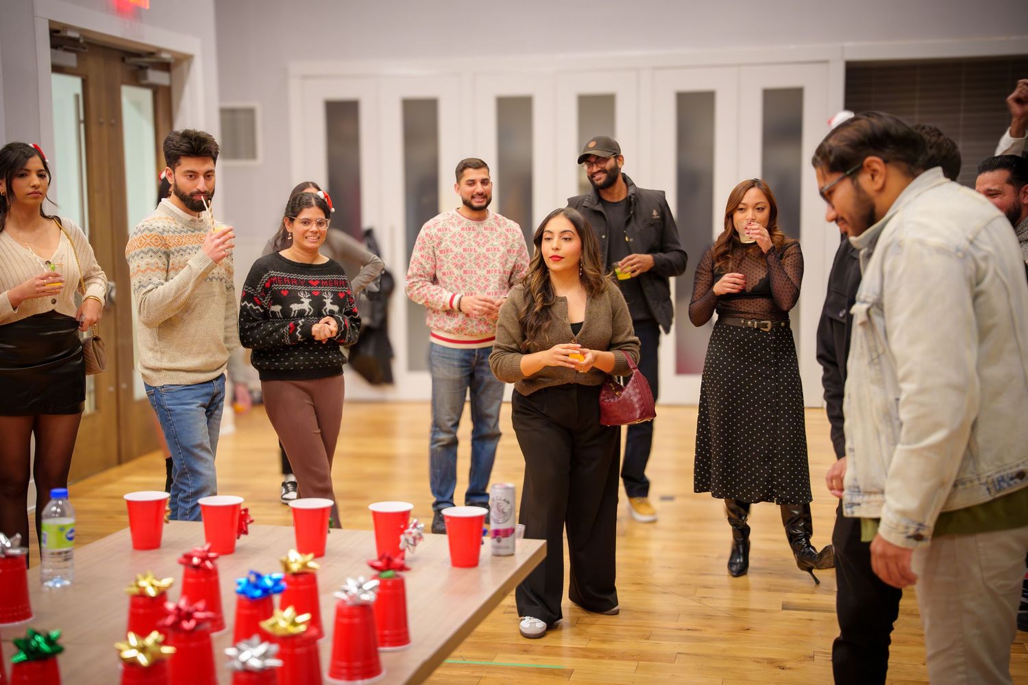 Red solo cups lined up on wooden floor for party games with people standing around.
