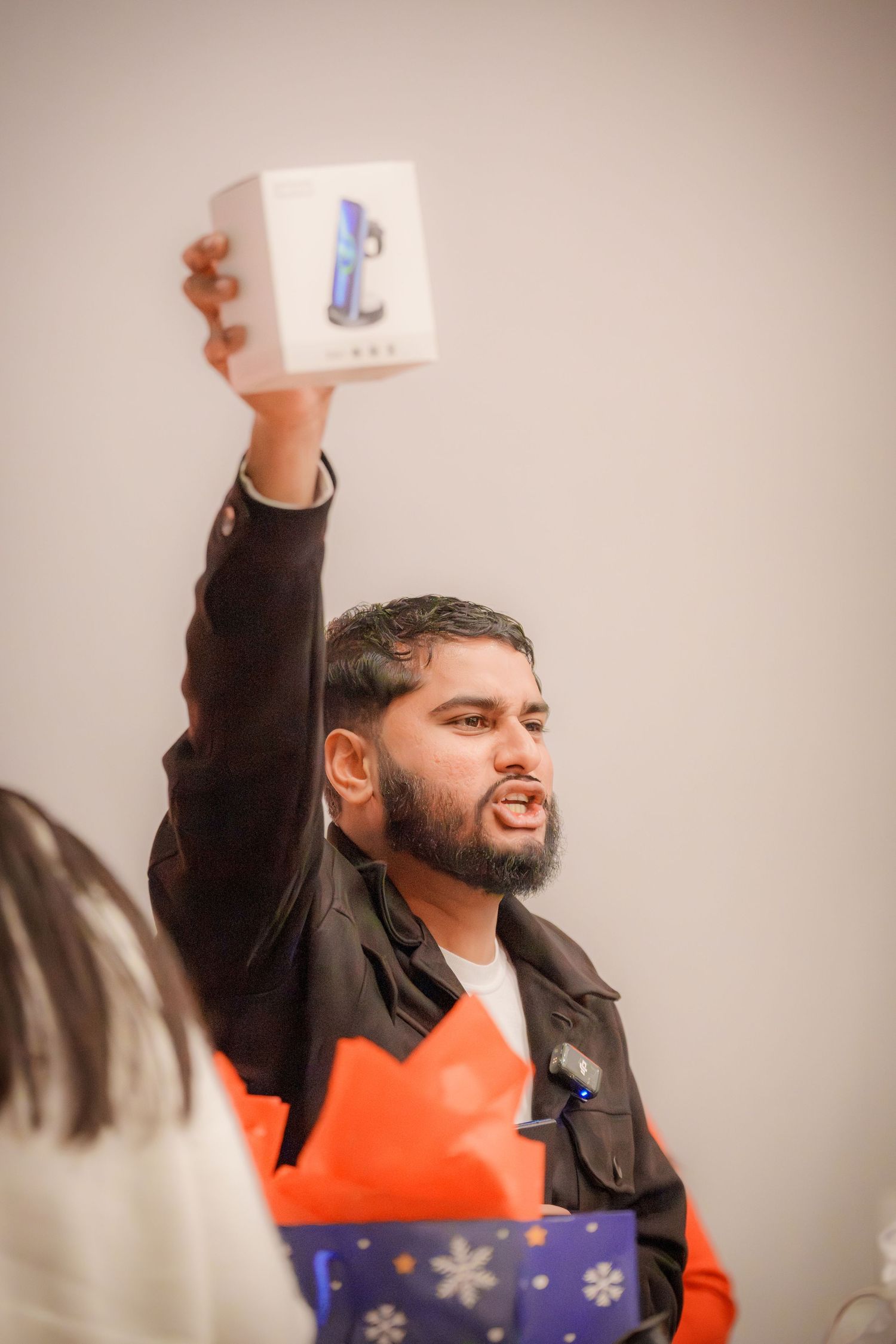 A person in a dark jacket raises their arms enthusiastically while holding a small box.