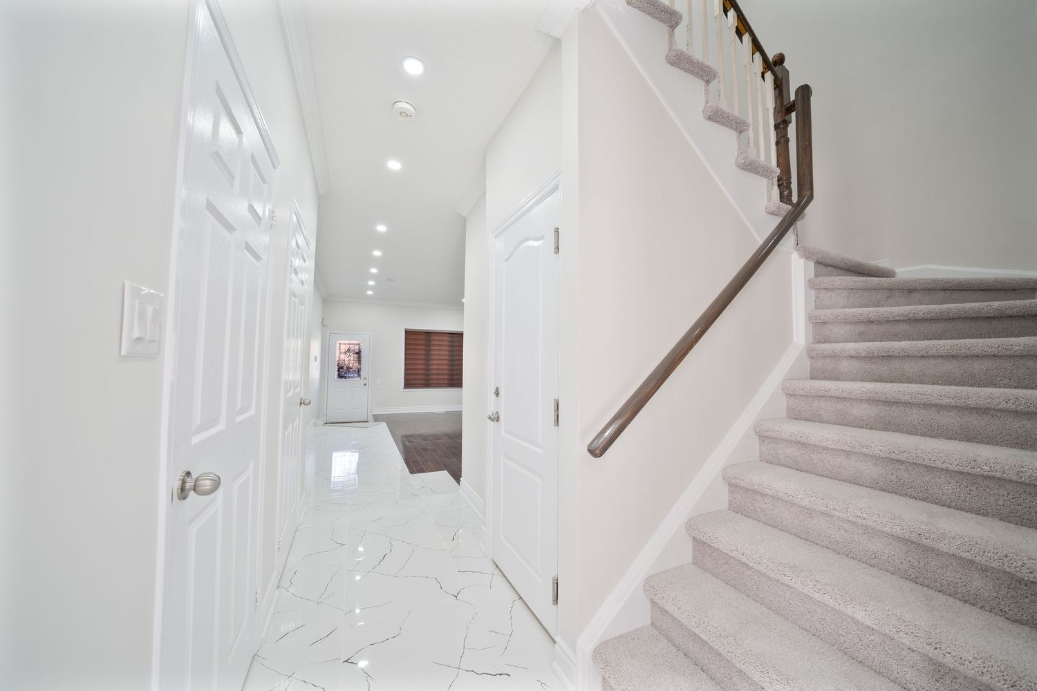 Modern white staircase with wooden handrail and recessed lighting in a contemporary residential hallway.