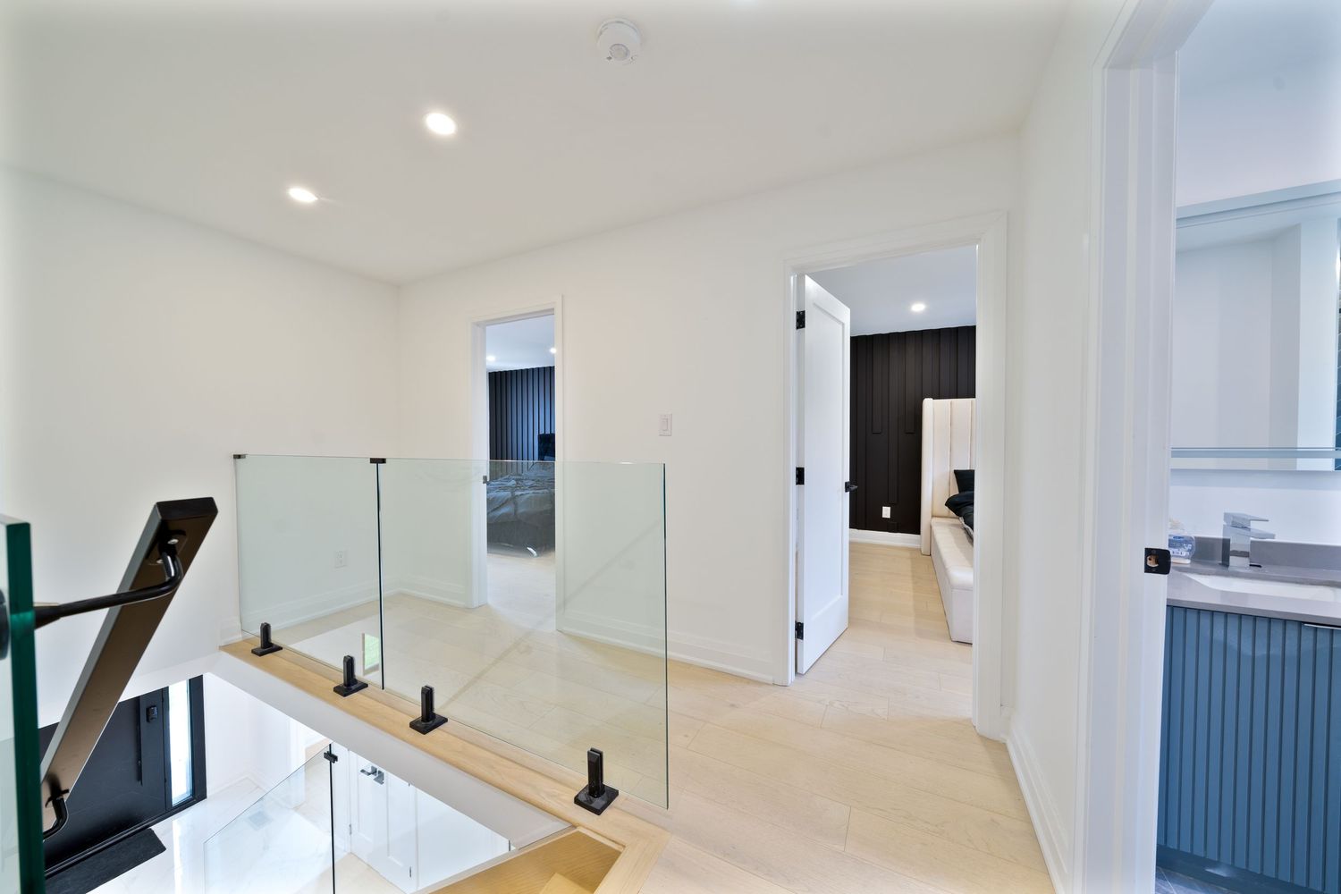 Modern white staircase with glass railing and dark metal posts leads upward in a bright minimalist interior.