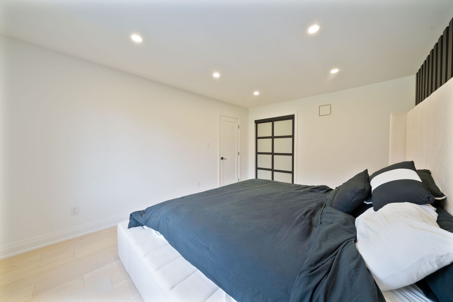 Modern bedroom interior with white walls, recessed lighting, and dark accent panels creating a sleek contemporary design.