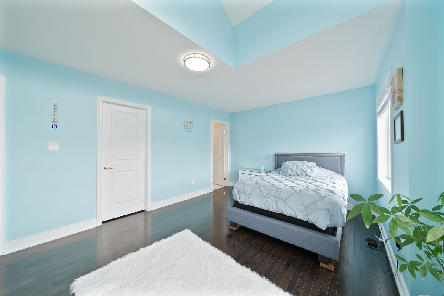 Modern bedroom with light blue walls, white trim, recessed lighting and hardwood floors features minimalist decor.