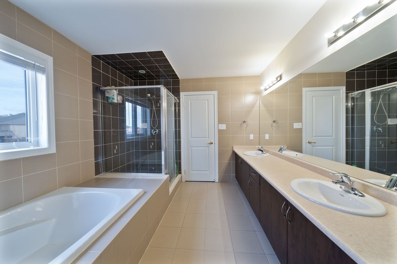 Modern bathroom with beige walls, black tile accents, and a large white vanity with dual sinks and mirror.