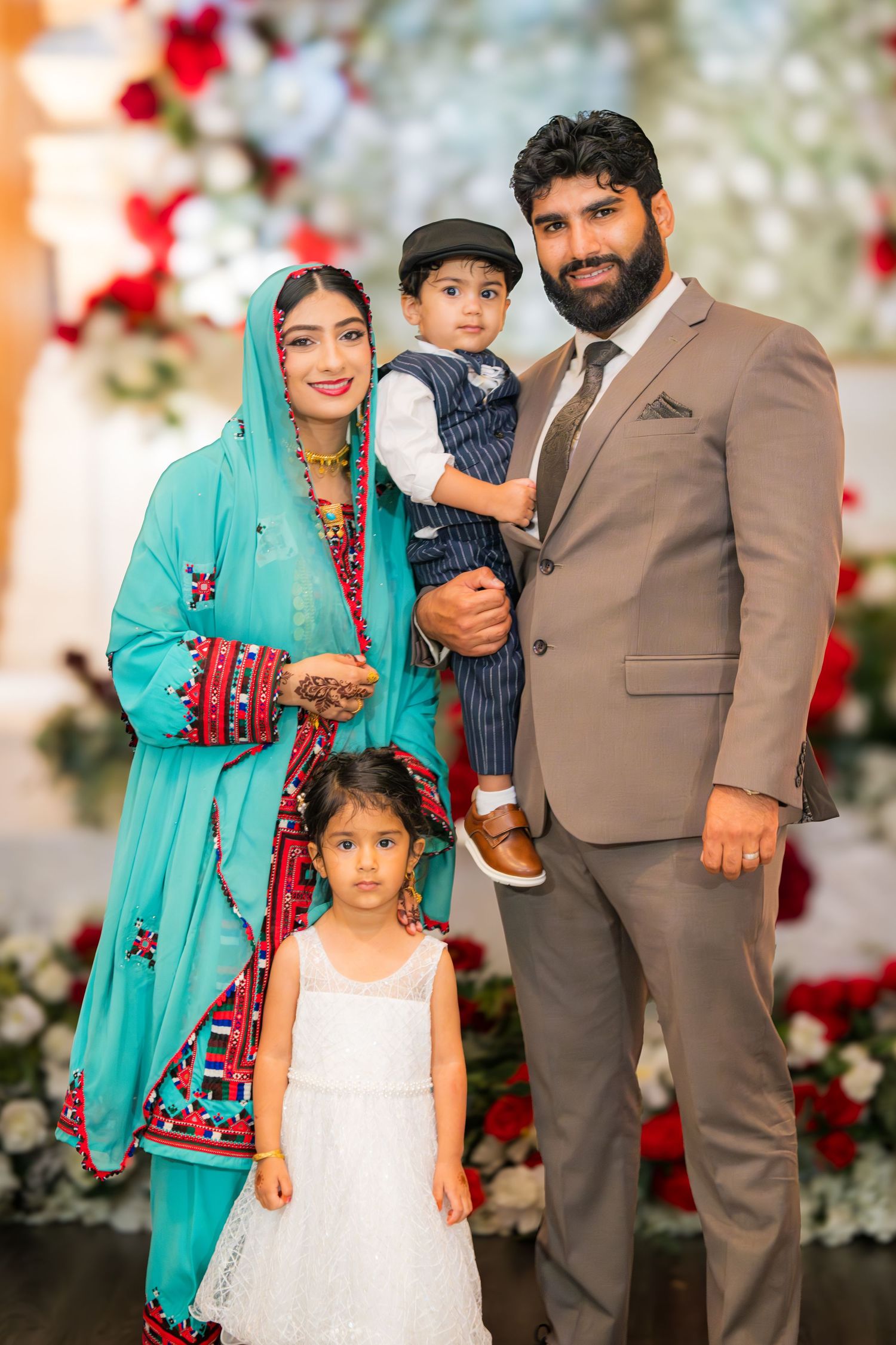 Family portrait session with vibrant turquoise and brown outfits against a red floral backdrop.