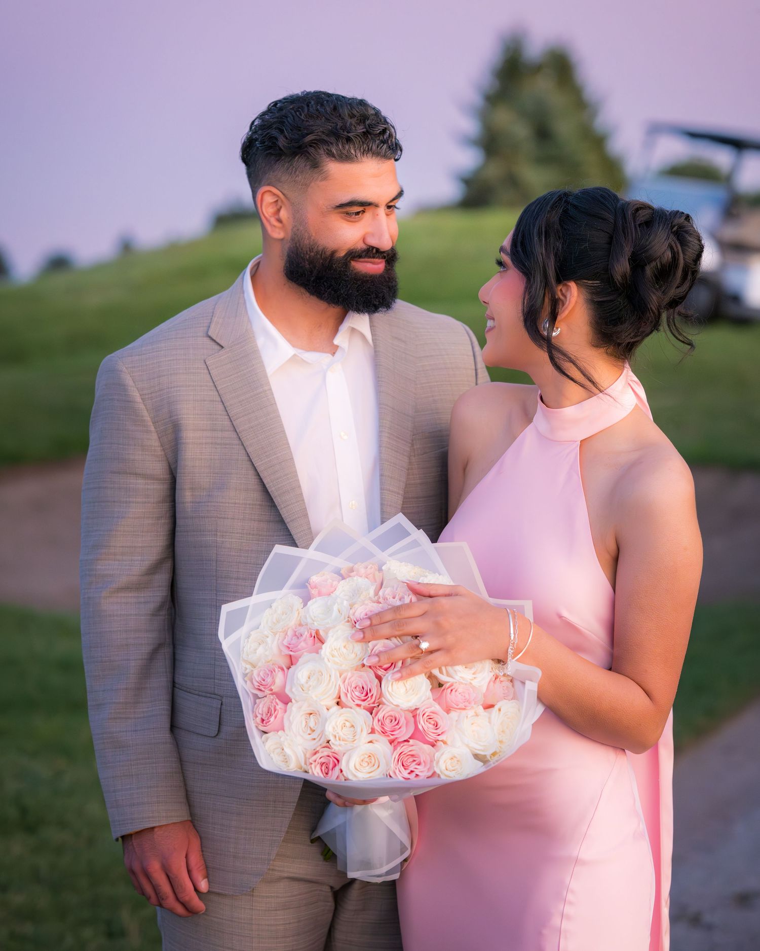 A couple shares an intimate moment while holding a bouquet of roses in an outdoor setting.