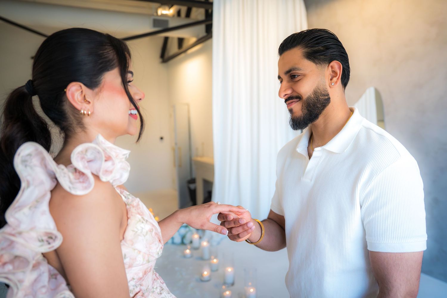 Man placing engagement ring on woman's finger in an elegant candlelit proposal setting.