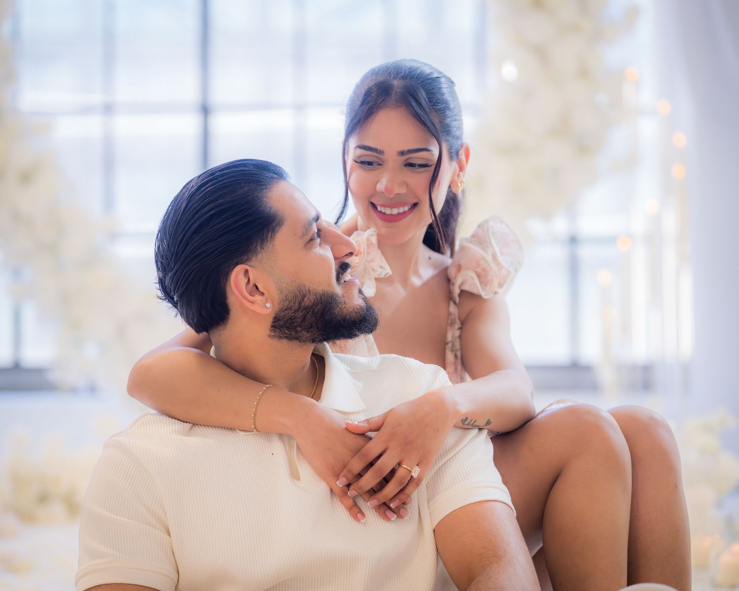 Smiling couple sharing romantic moment surrounded by white floral decorations.