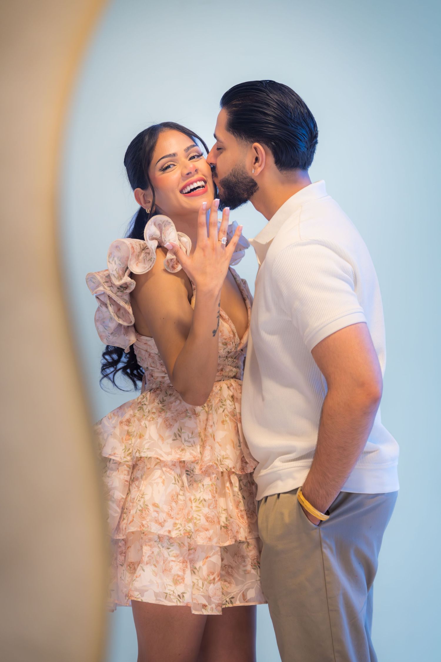 Laughing bride-to-be displaying engagement ring while partner whispers in her ear.