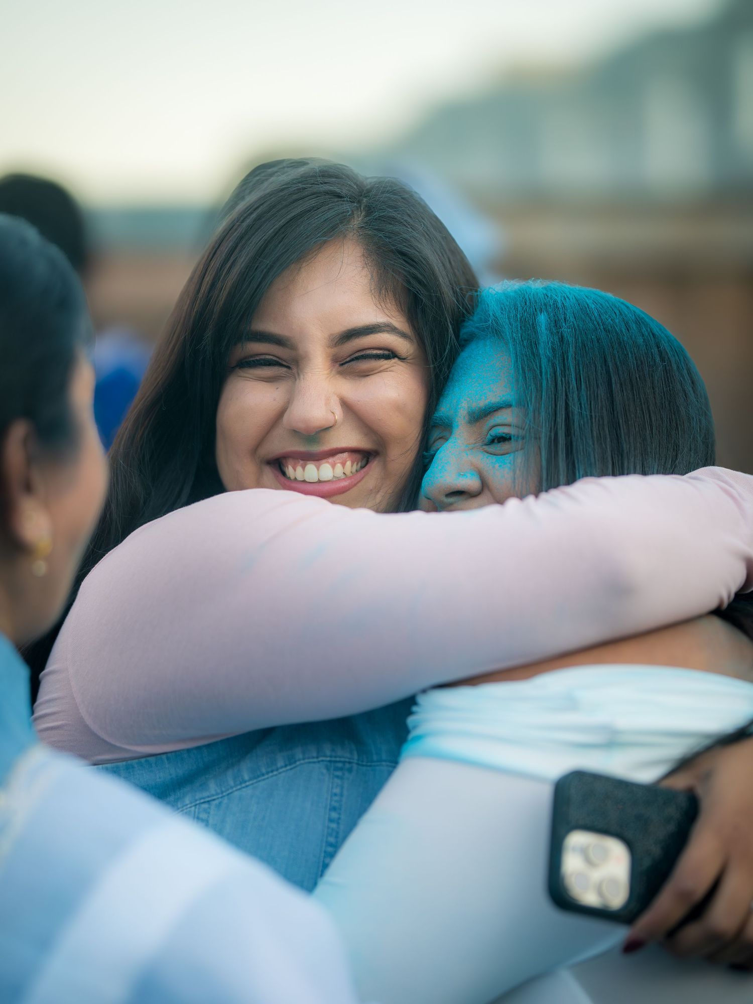 Two women hugging joyfully, one covered in blue powder at a gender reveal celebration.