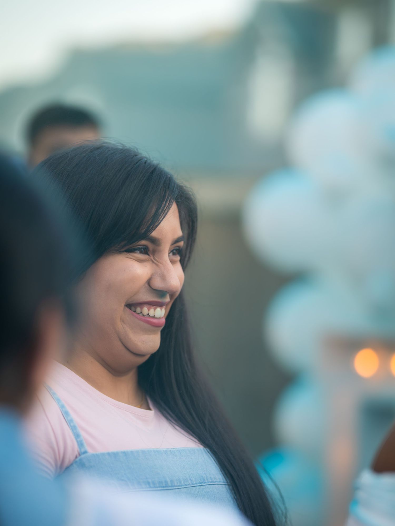A smiling woman with long dark hair enjoys a festive outdoor party with blue balloons.