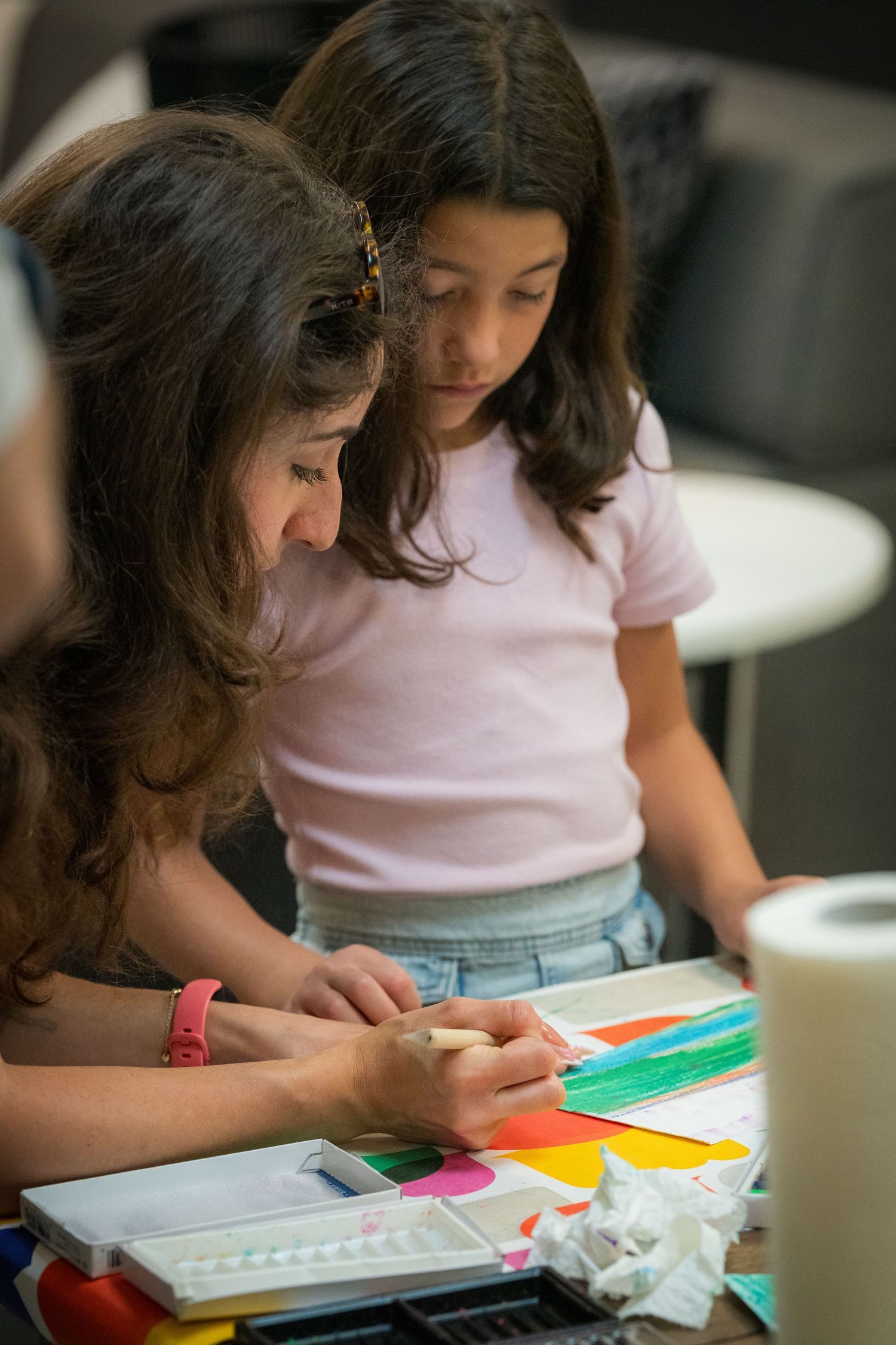 Two girls focused on a colorful art project at a table with paints and bright paper.