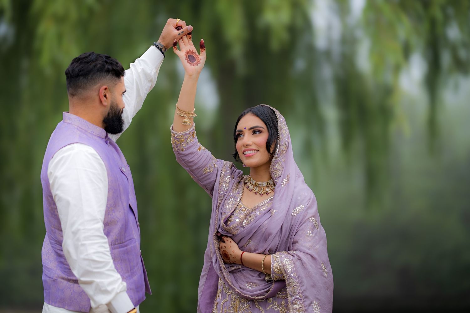 A couple in coordinated purple outfits dance together in a romantic outdoor setting.