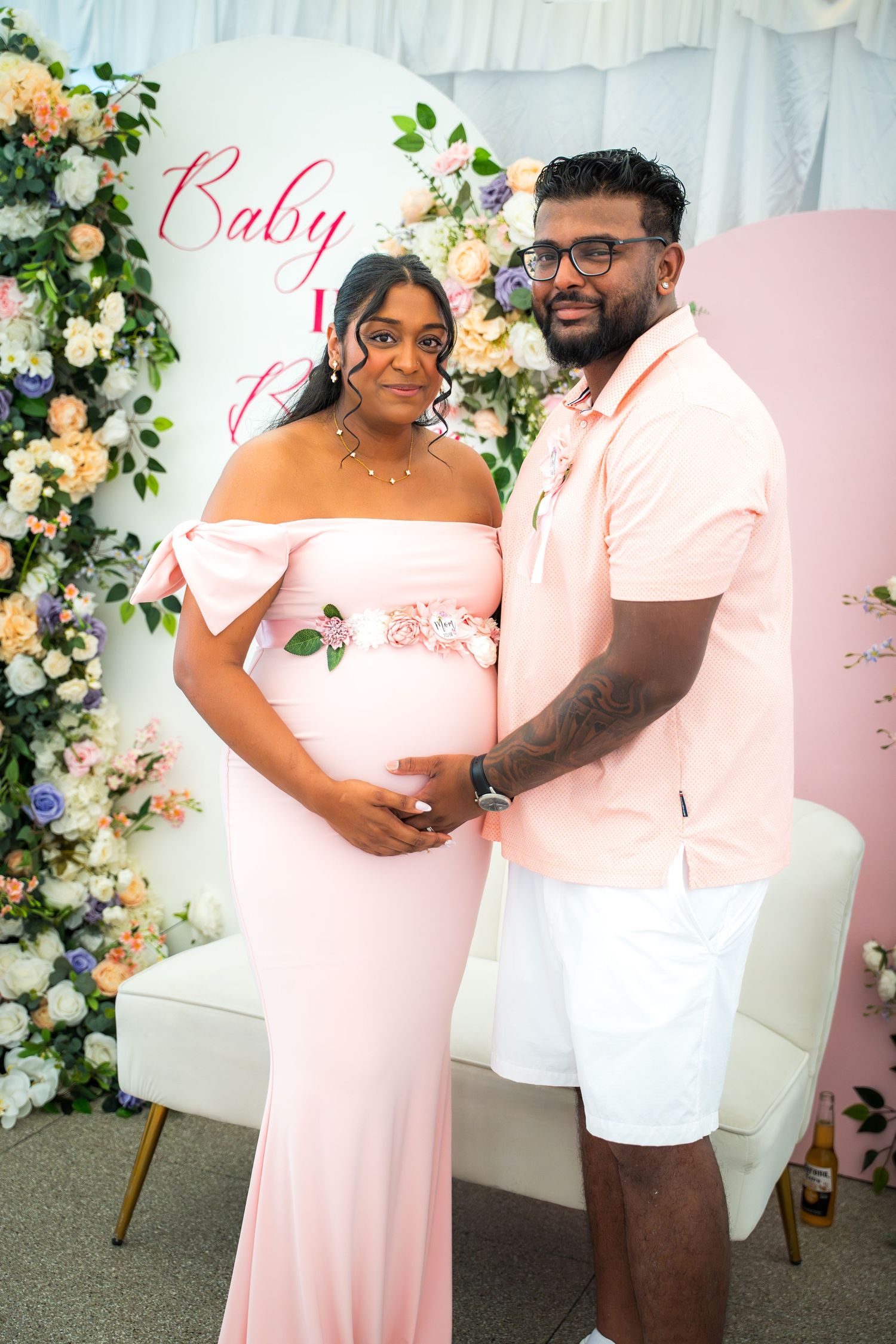 Expecting parents celebrating at baby shower with elegant floral backdrop and pink theme.
