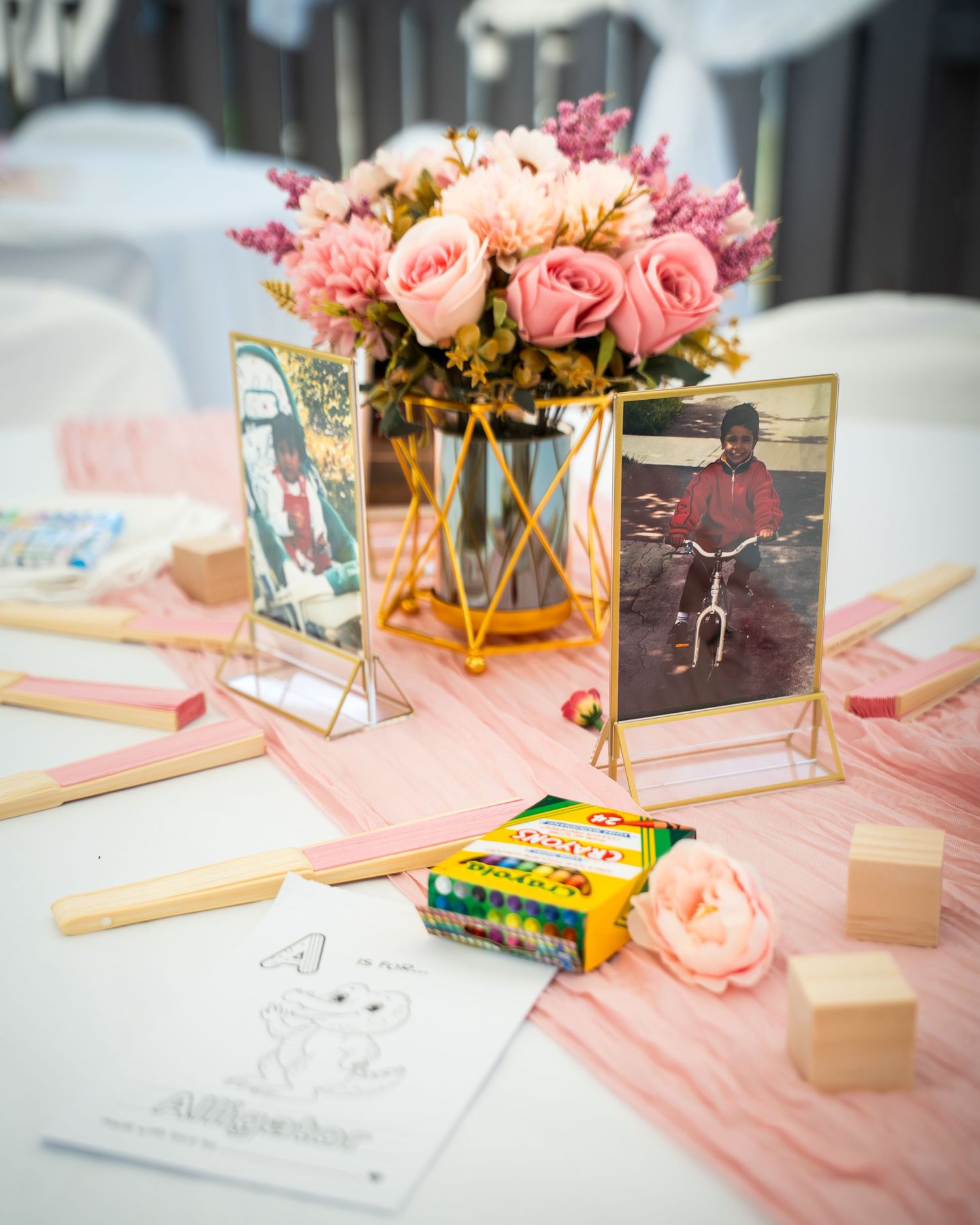 Pink table settings with gold frames and floral centerpieces at a baby celebration.