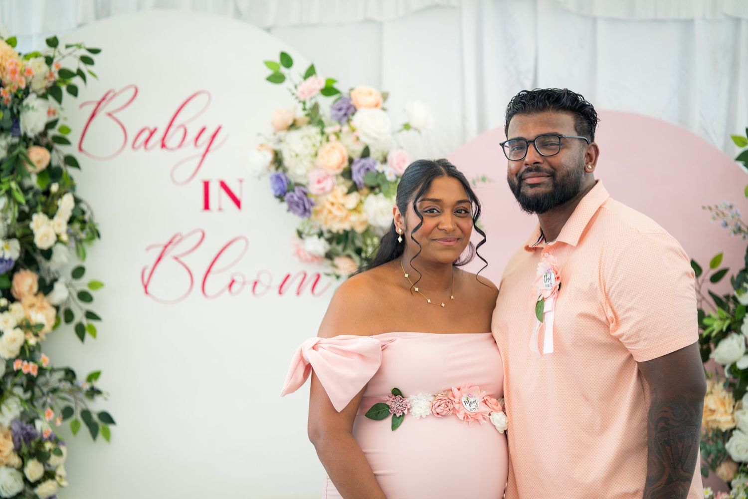 Baby shower celebration with pink decor, white draping, and floral arrangements.