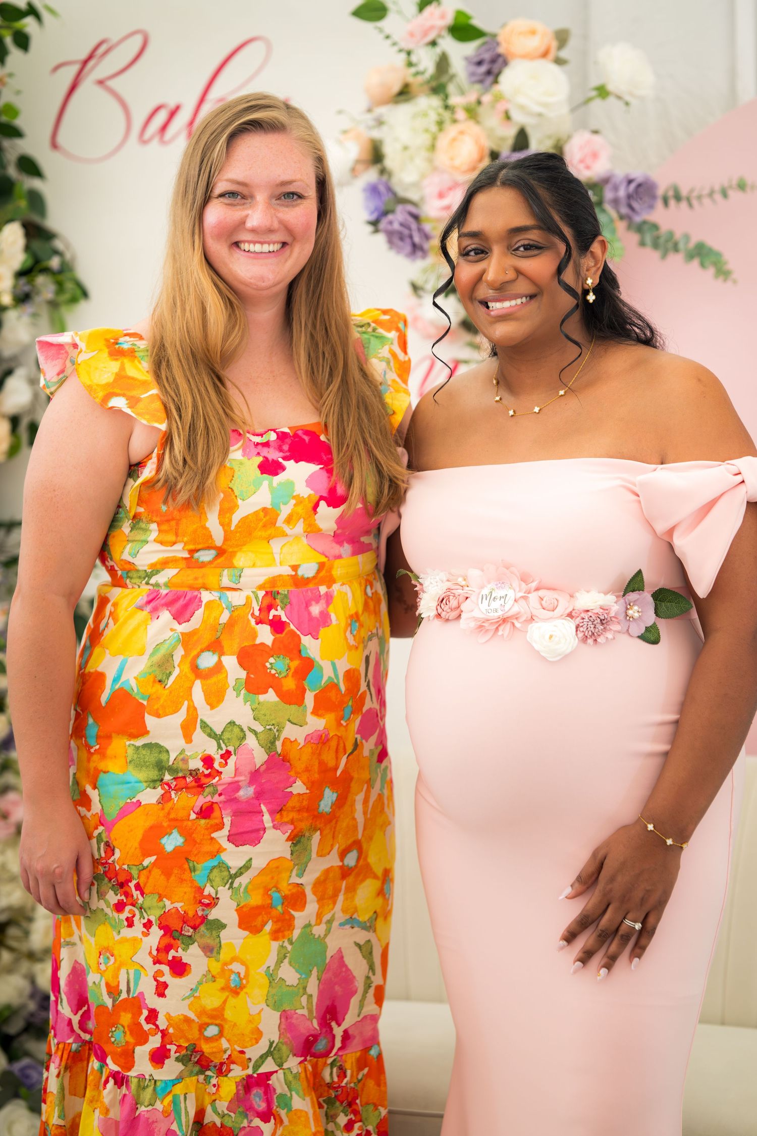 Two guests pose together, one wearing a bright floral dress and one in pink.