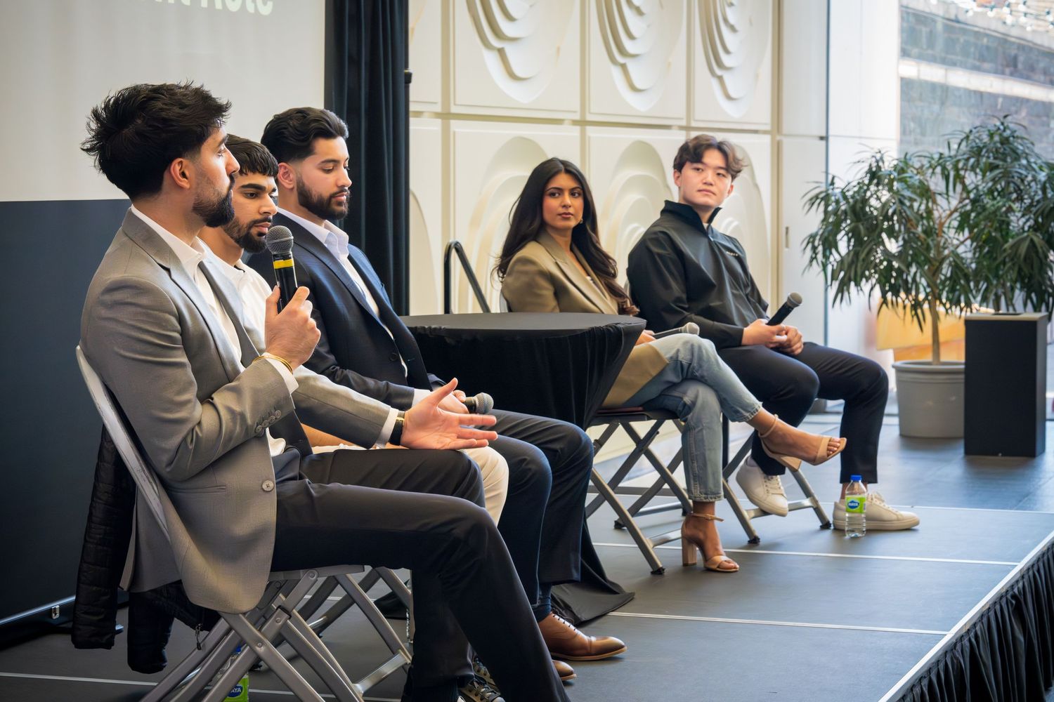 Panel discussion participants seated in folding chairs engage in conversation during a professional event.