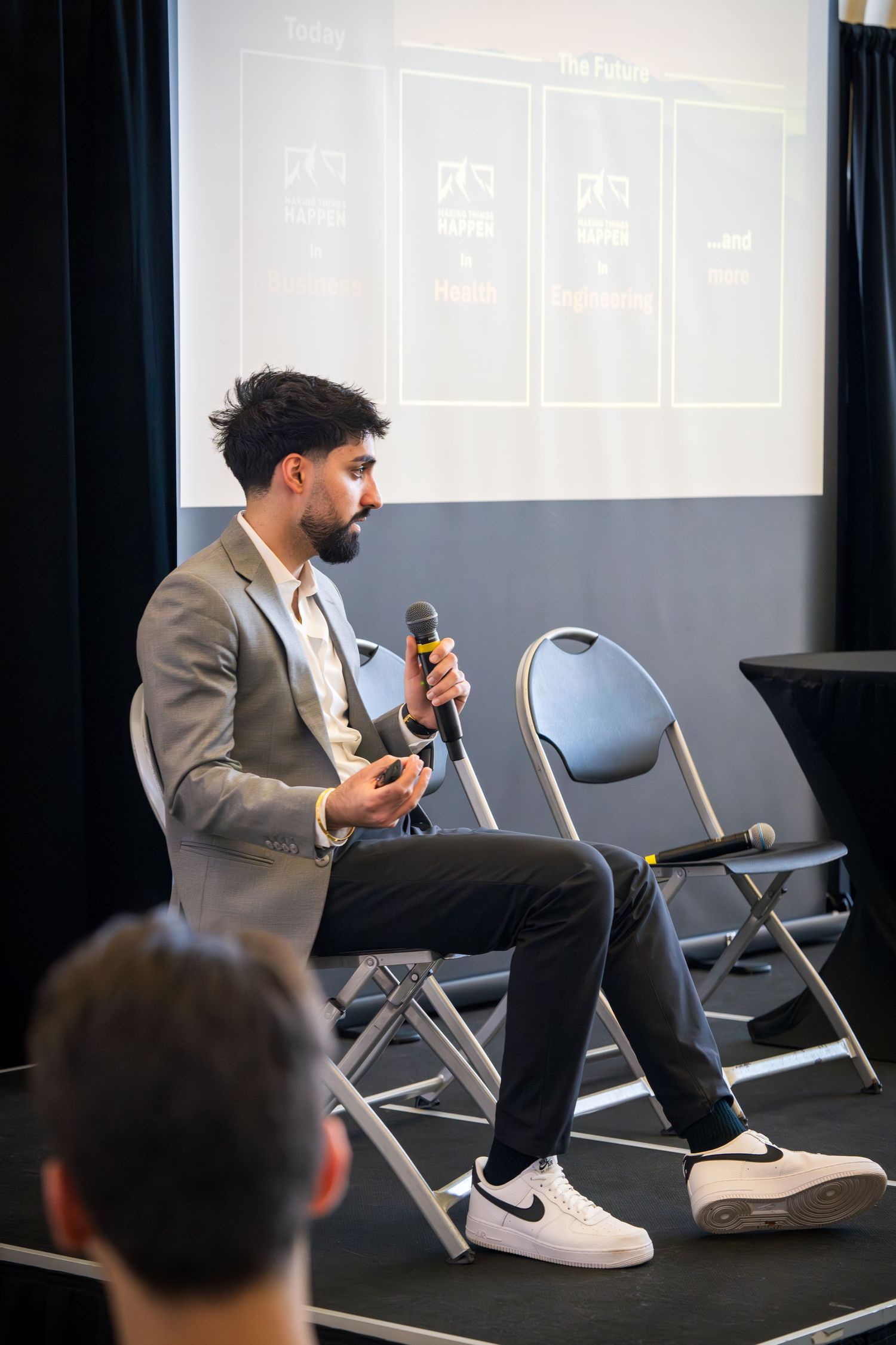 Business presenter speaking into microphone while seated on stage during conference.