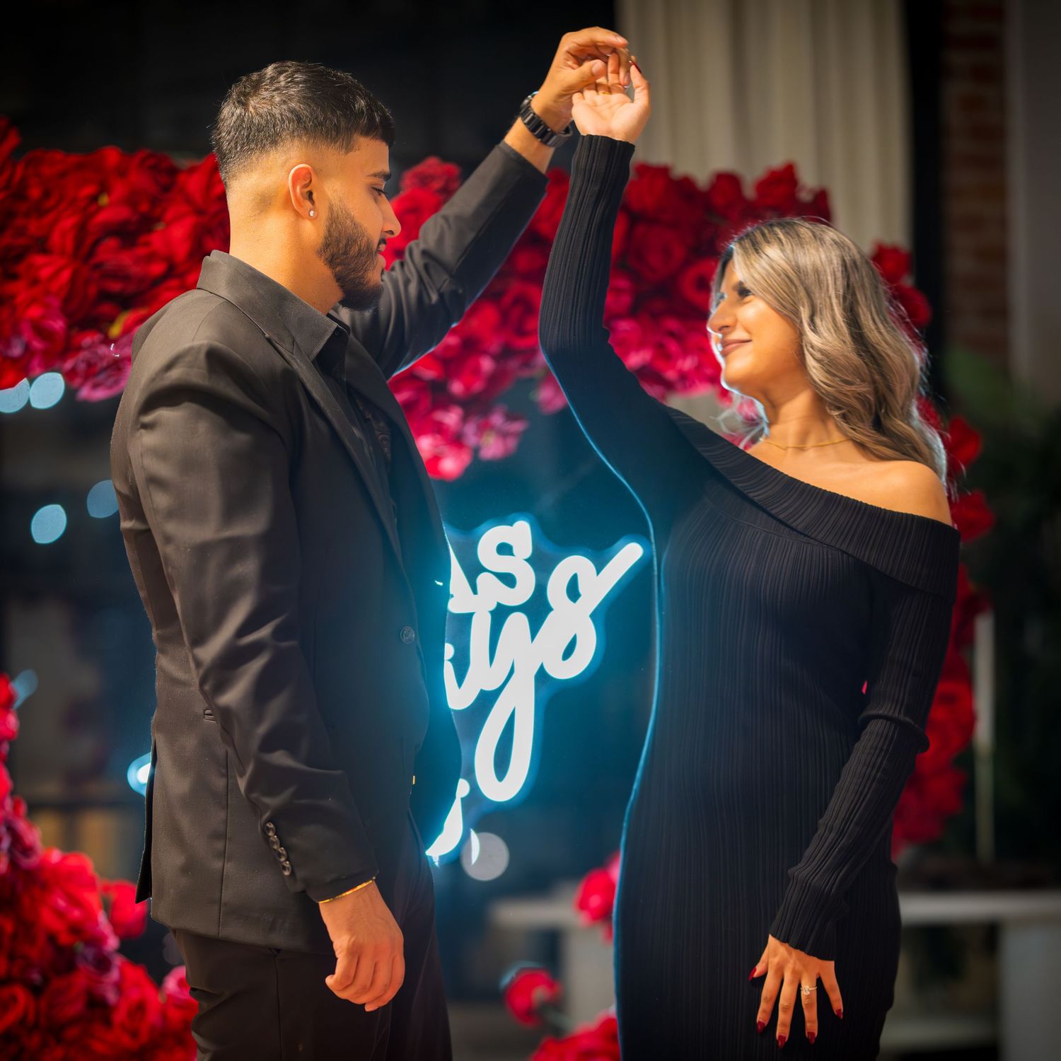 A couple sharing a romantic dance moment surrounded by red roses and neon lighting.