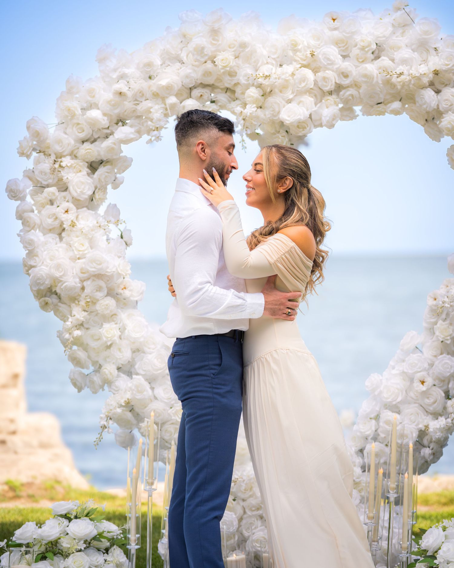 Wedding ceremony setup with white floral arch and ocean view backdrop.