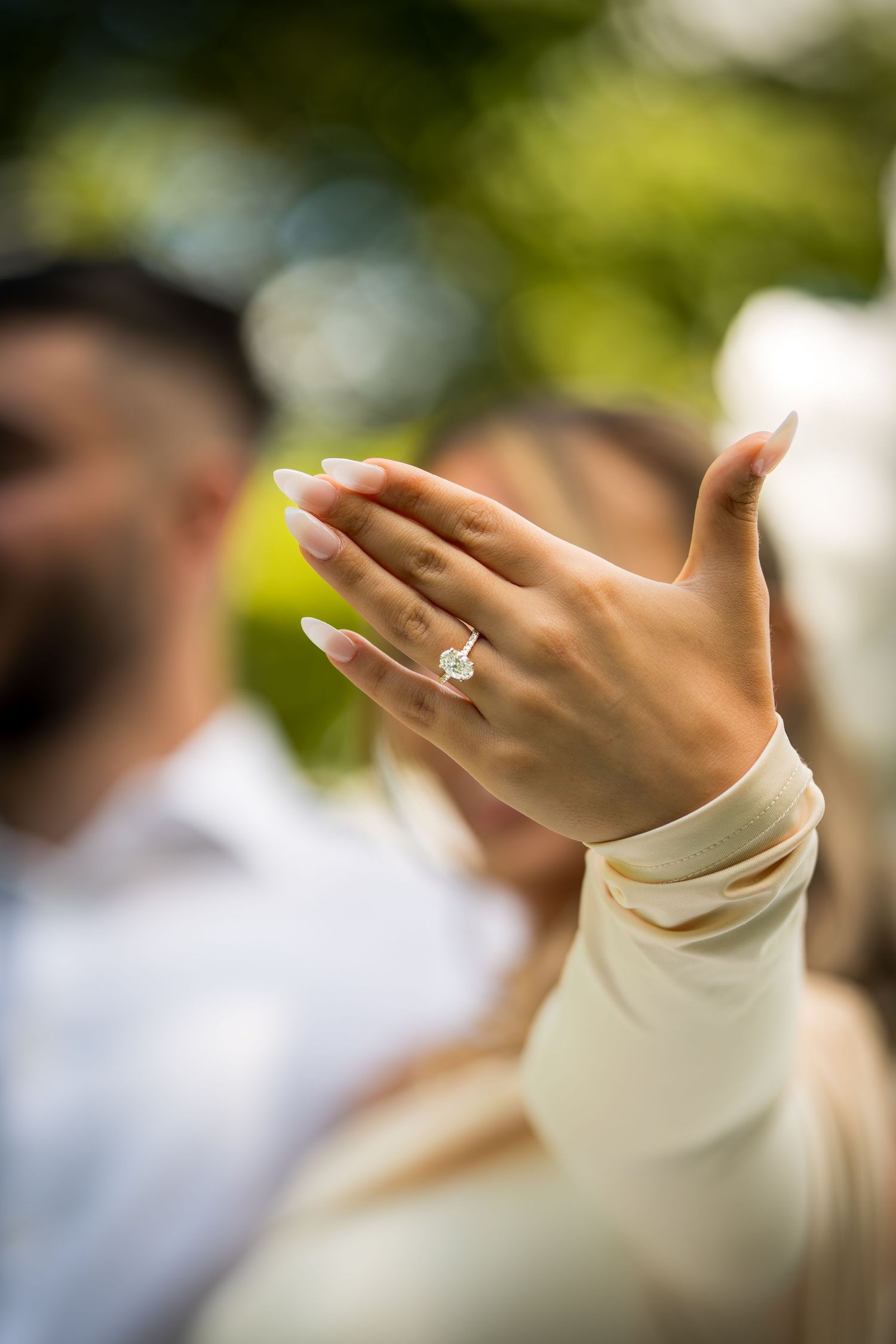 Close-up shot of an engagement ring on a hand against a blurred natural background.